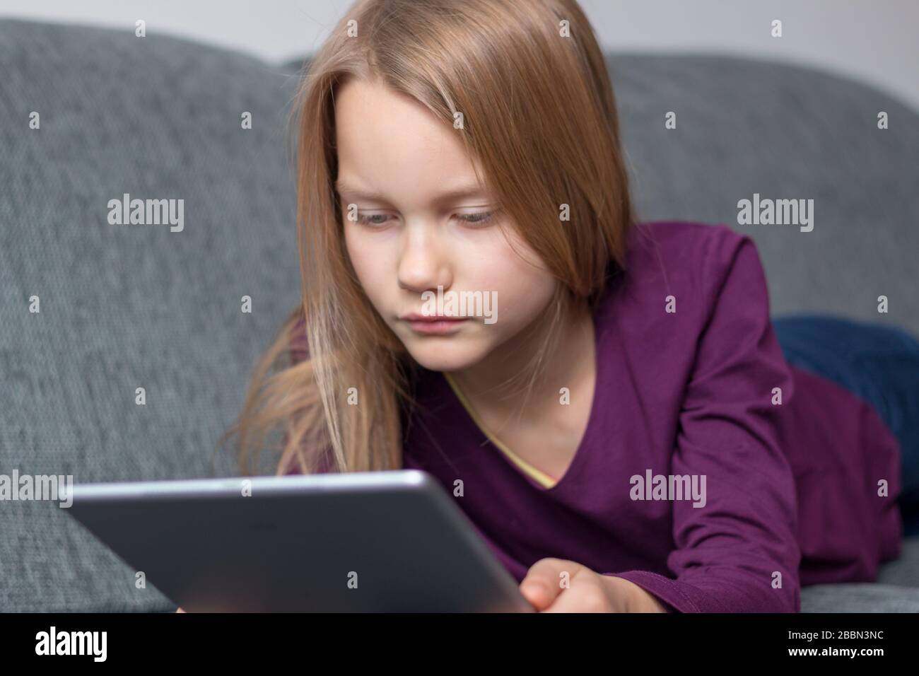 Mädchen liegt auf dem Sofa und schaut auf einen Tablet-Computer Stockfoto