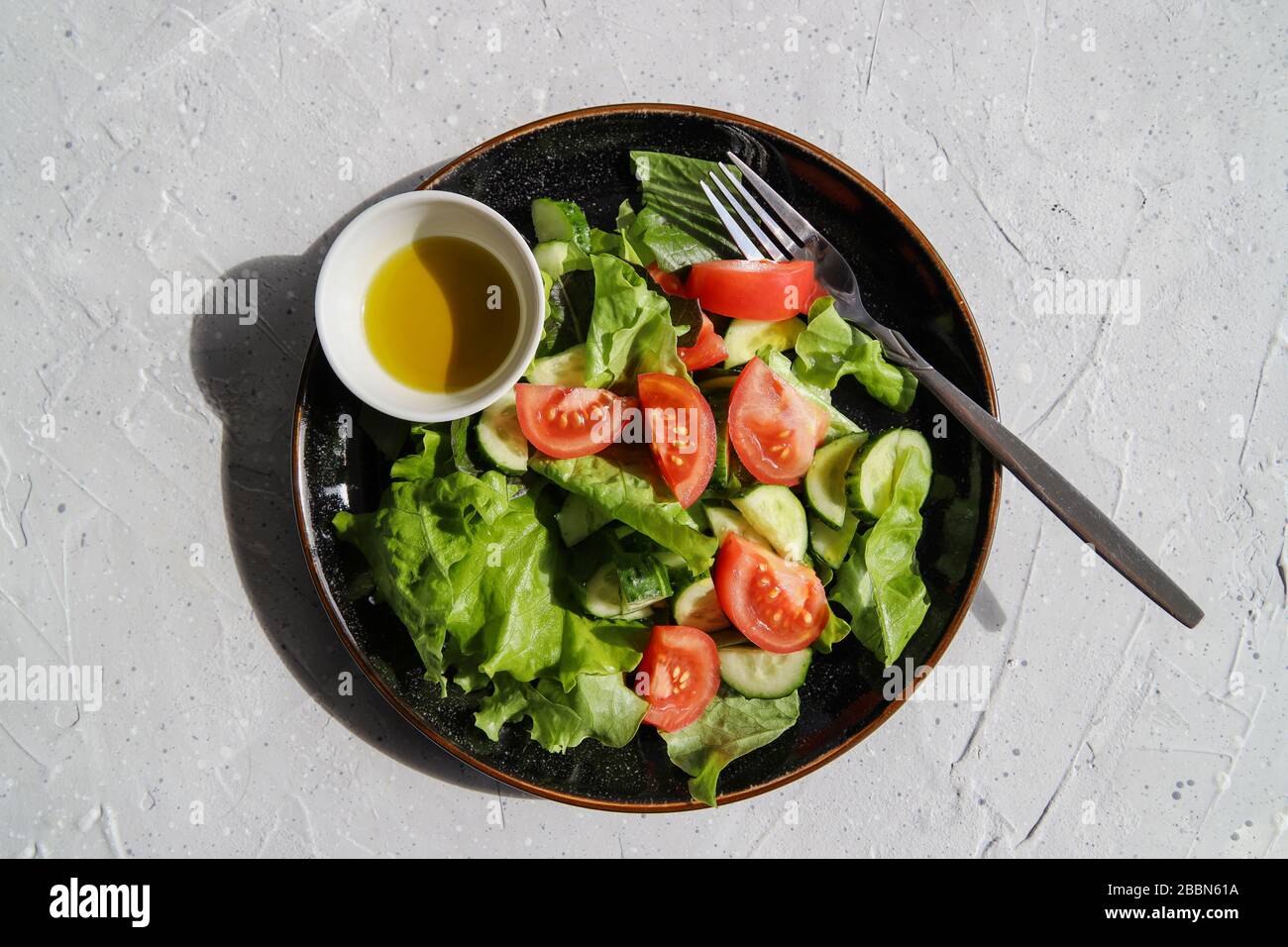 Frischer Detox-Salat im Sommer mit Tomaten, Gurke, Romain-Salat und Olivenöl auf grauem Betongrund. Gesunde Ernährung für Veganer oder Vegetarier Stockfoto