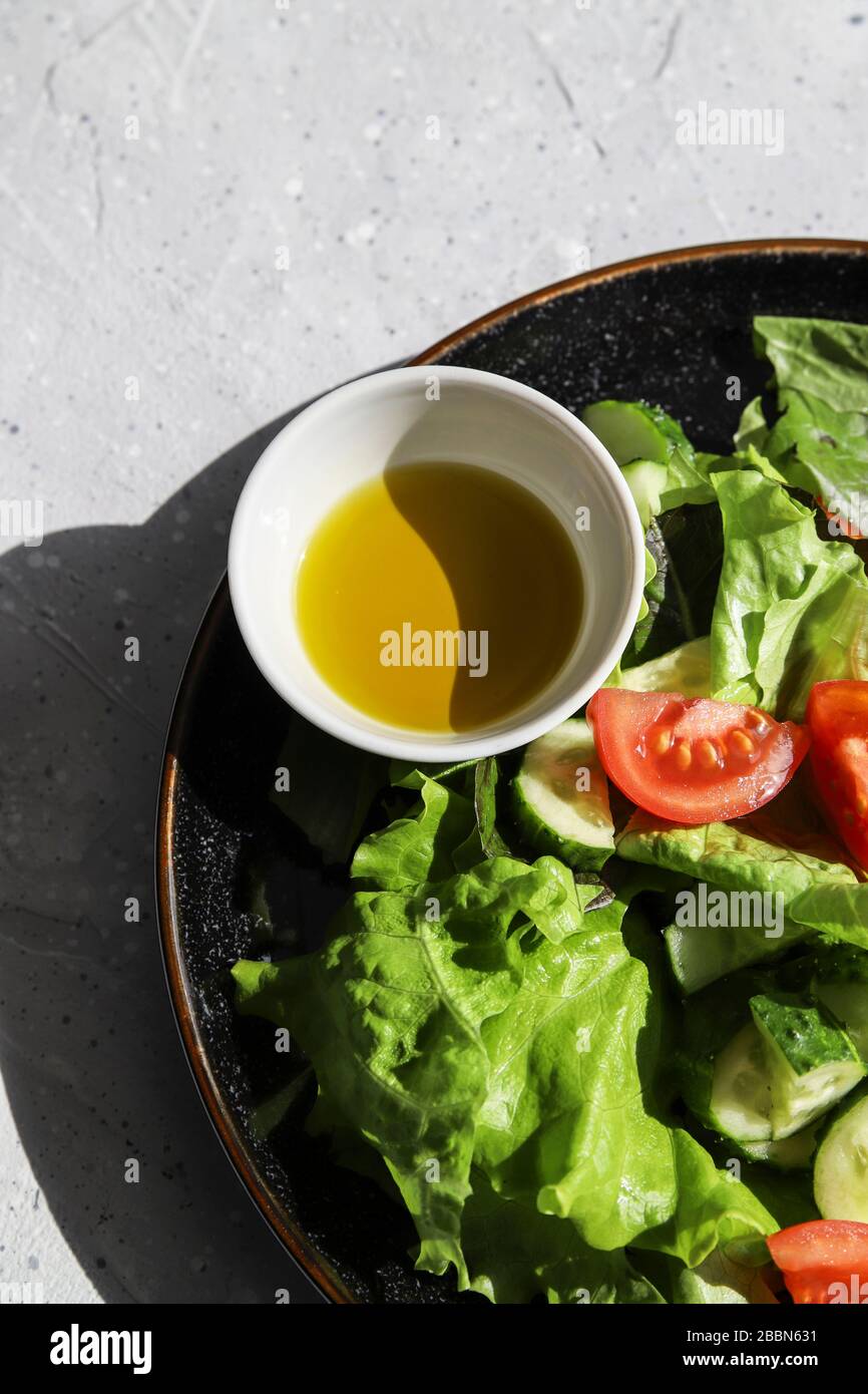Frischer Detox-Salat im Sommer mit Tomaten, Gurke, Romain-Salat und Olivenöl auf grauem Betongrund. Gesunde Ernährung für Veganer oder Vegetarier Stockfoto