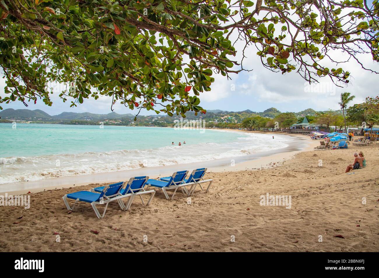 Castries, St. Lucia - 8. Februar 2020: Tourist am Vigie-Strand - Menschen unter FLIESSENDEN gesponserten Sonnenschirmen, Paar auf Sand sitzend, liegen. Stockfoto