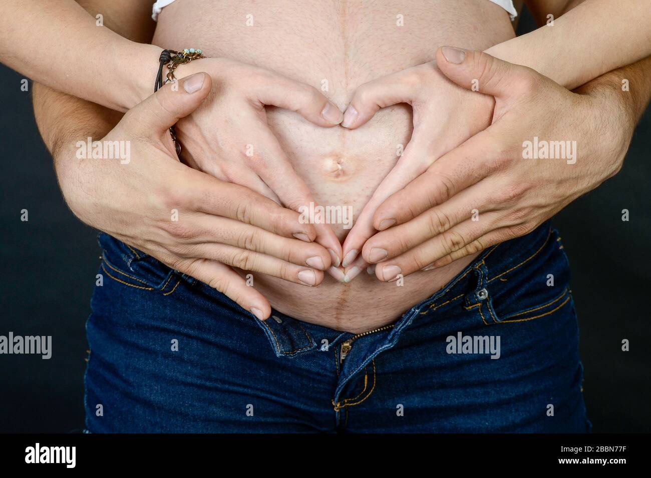 Die Hände des Vaters und der Mutter auf dem schwangeren Bauch der Frau Zeigt die Herzform an Stockfoto