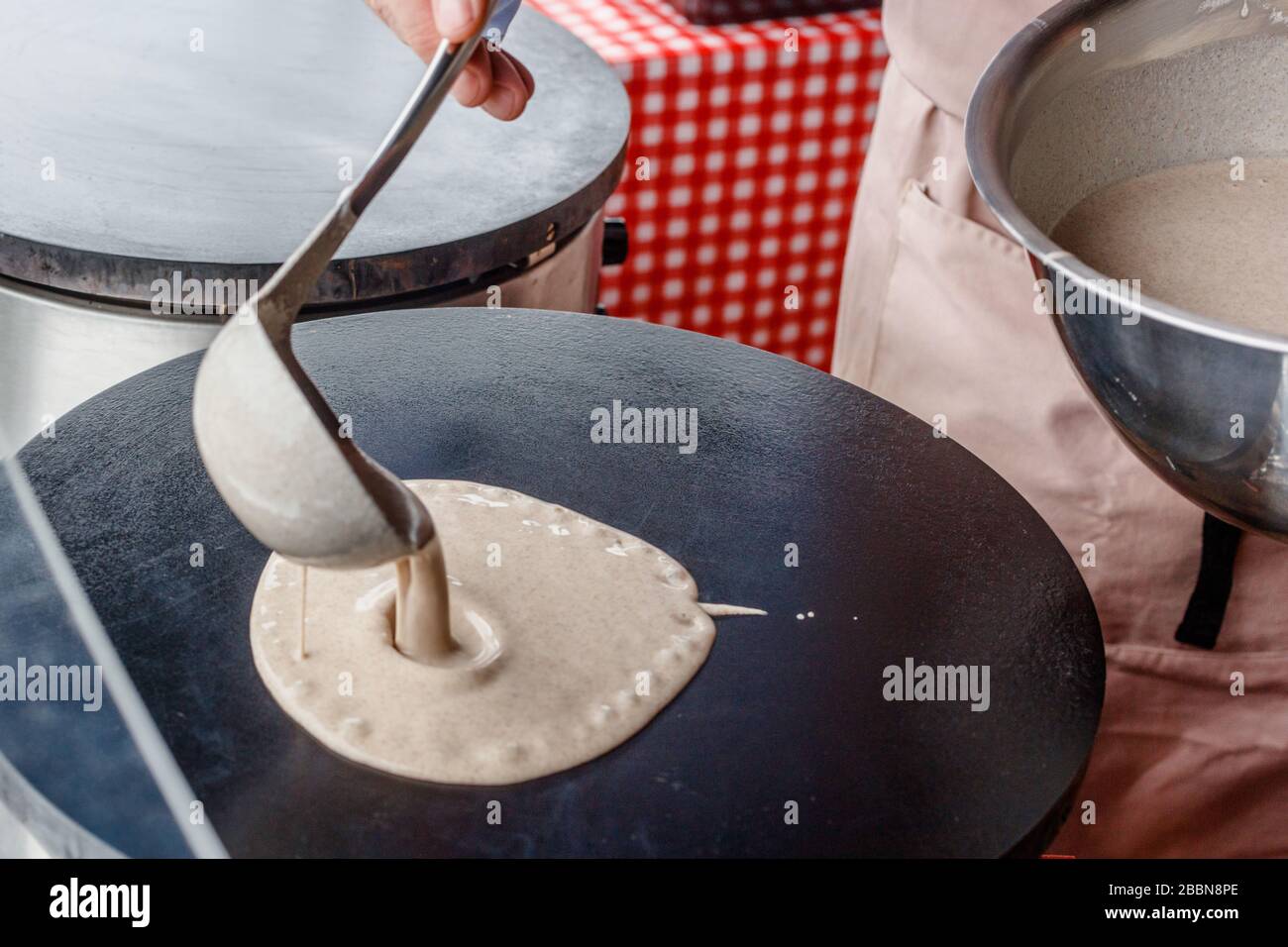 Crepes Pfannkuchen auf einem Lebensmittelmarkt machen. Eine Hand schüttet Schlagstöpsen auf einen Metallgriff im Freien Stockfoto