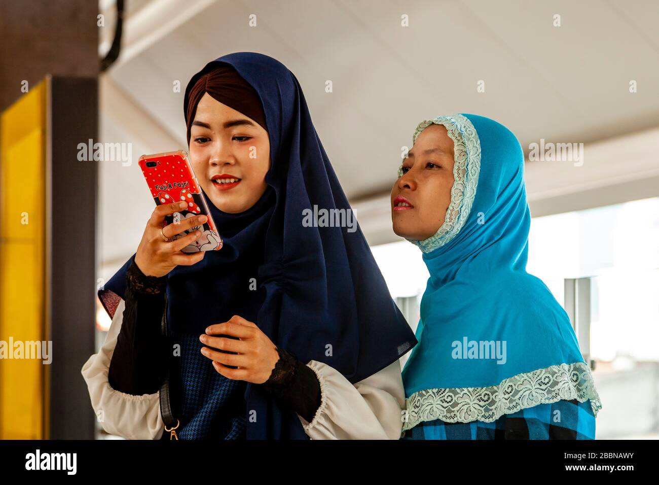 Zwei junge Frauen, die ein Smartphone (Handy), die Metro (MRT), Jakarta, Indonesien, suchen. Stockfoto