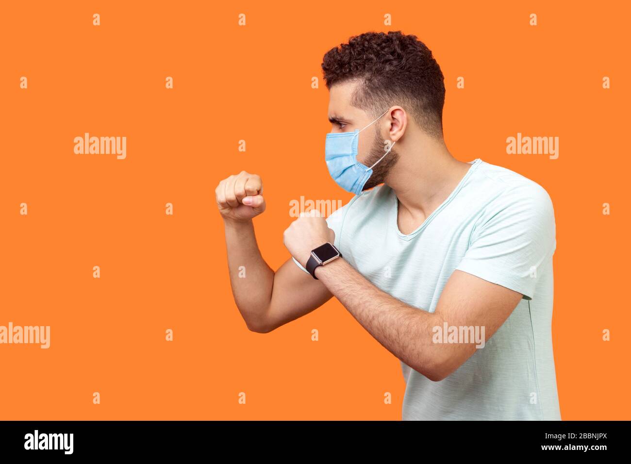 Boxen und Selbstverteidigung. Seitenansicht des aggressiven Mannes mit chirurgischer medizinischer Maske, die Fäuste zusammenhält, bereit für den Kampf. Leerer Kopierraum auf der linken Seite für Stockfoto