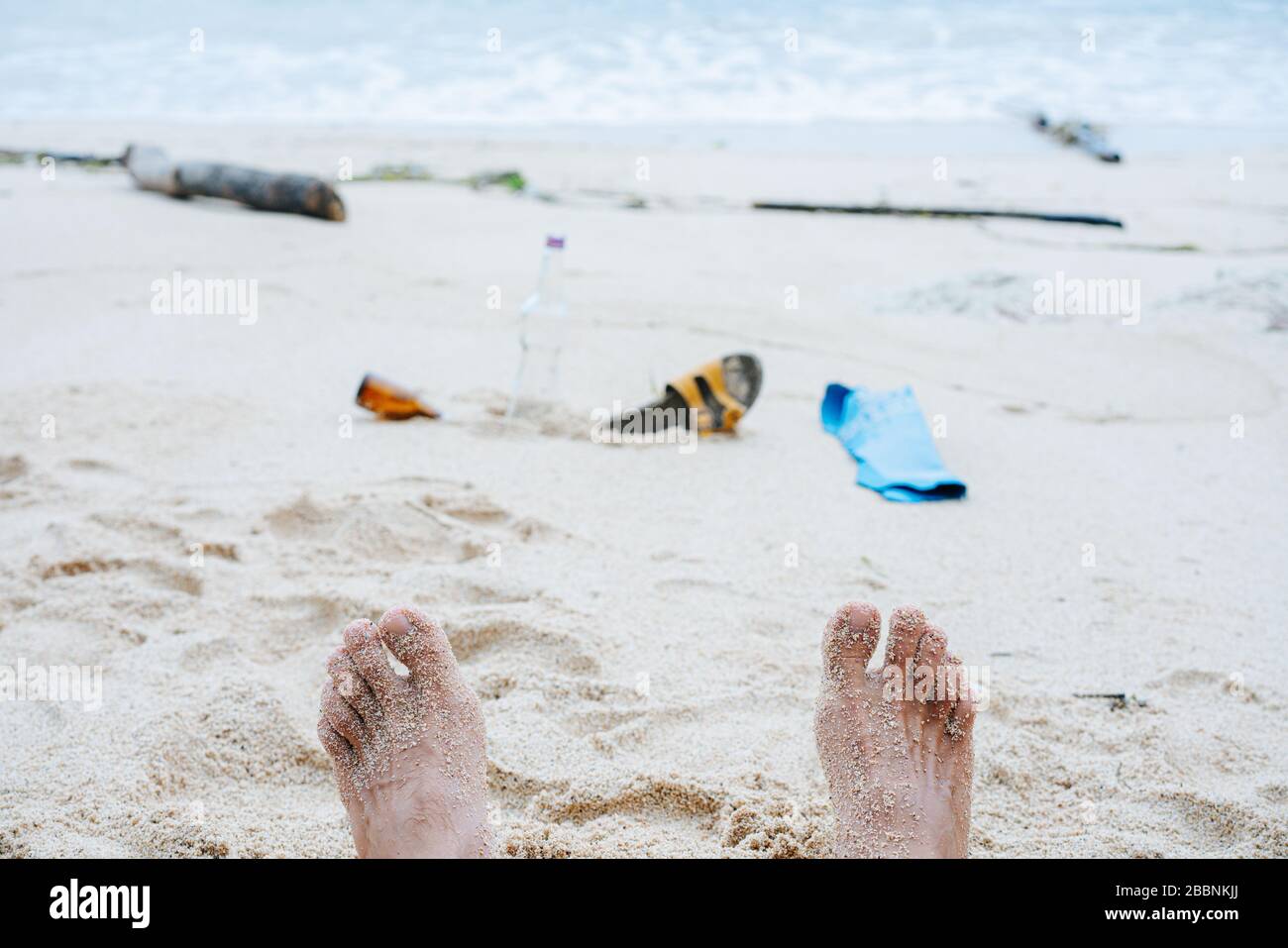 Sichtbild der Füße und des Mülls der Person auf Strandsand eines Ozeanufers Stockfoto