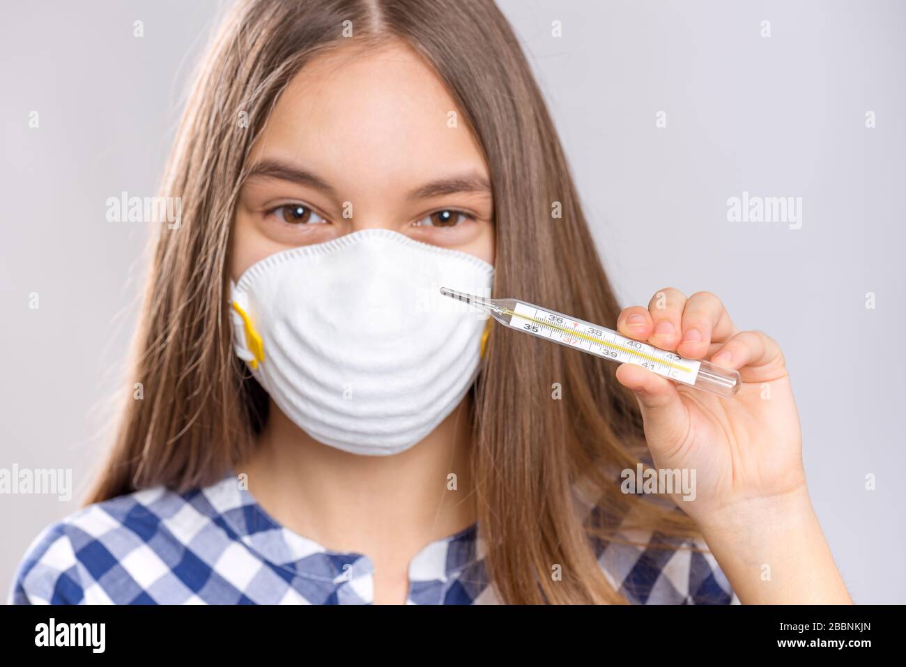 Konzept der Quarantäne von Coronavirus. Happy Child trägt eine medizinische Schutzmaske, die Thermometer bei normaler Temperatur hält. COVID-19. Gesundes Lächeln Stockfoto