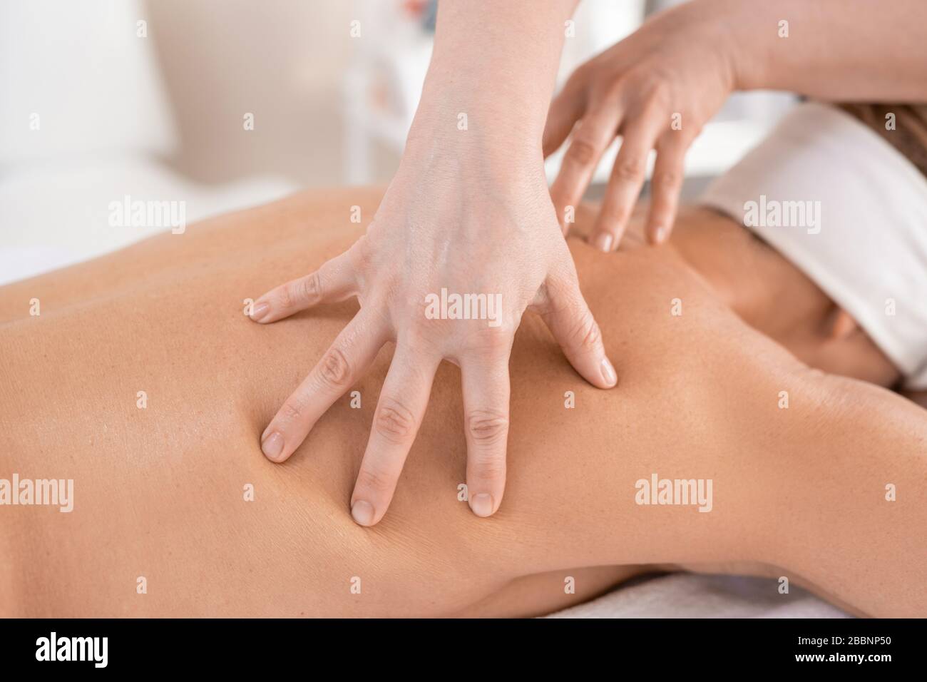 Nahaufnahme des Massagetherapeuten, der die Rückenmuskeln der Frau verwöhnt, während er im Spa-Salon eine manuelle Massage durchführt Stockfoto