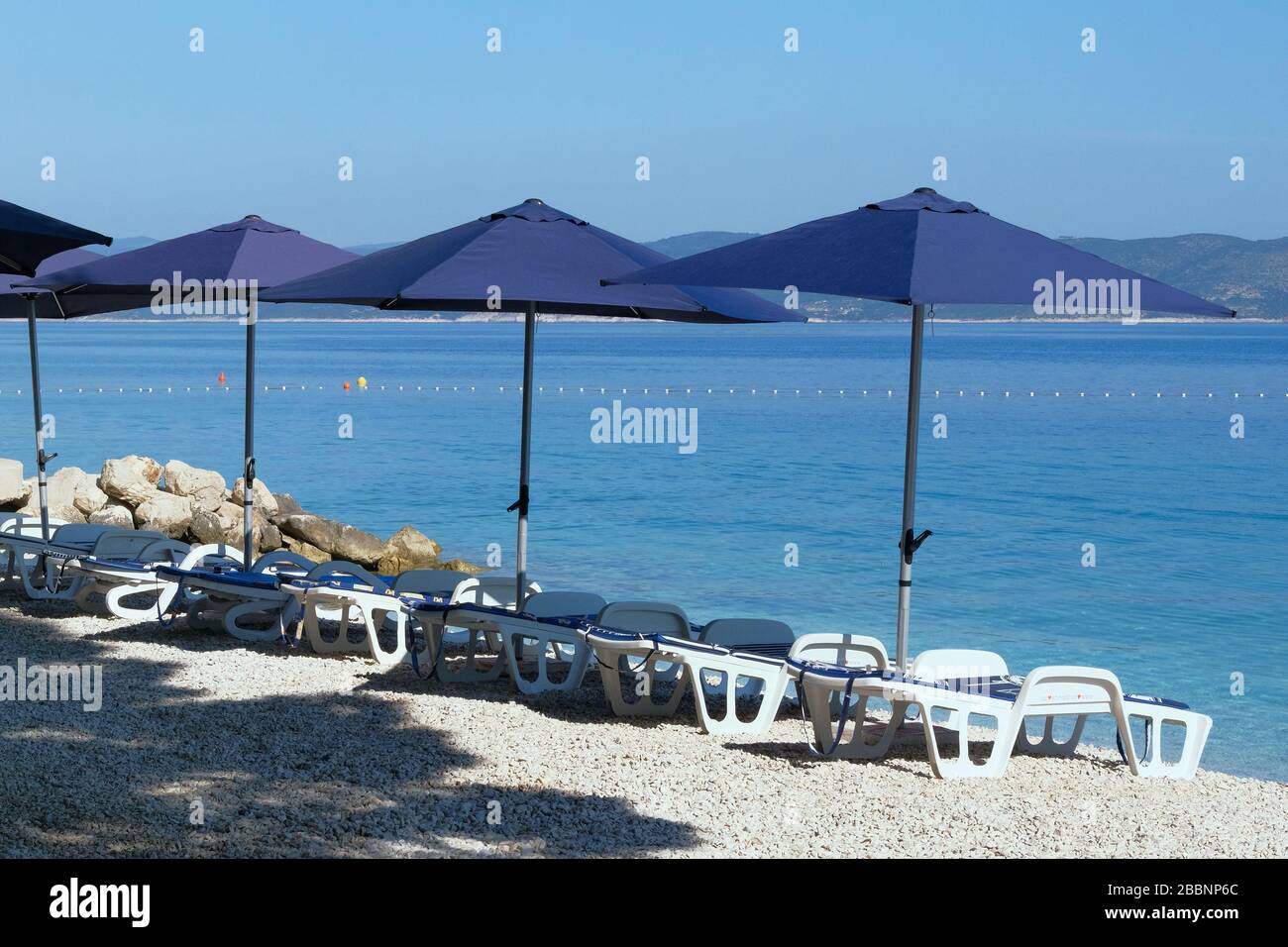 Blaue Sonnenschirme und Chaise für Entspannung und Komfort am Strand. Fröhlicher Sommerurlaub und Tourismuskonzept. Kostenpflichtiger Service an Stränden mit Wasserlandschaft. Stockfoto