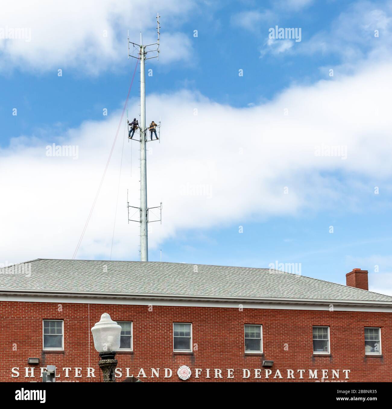 Zwei Männer, die an einem Funkturm über der Shelter Island Fire Department in Shelter Island, NY arbeiten Stockfoto