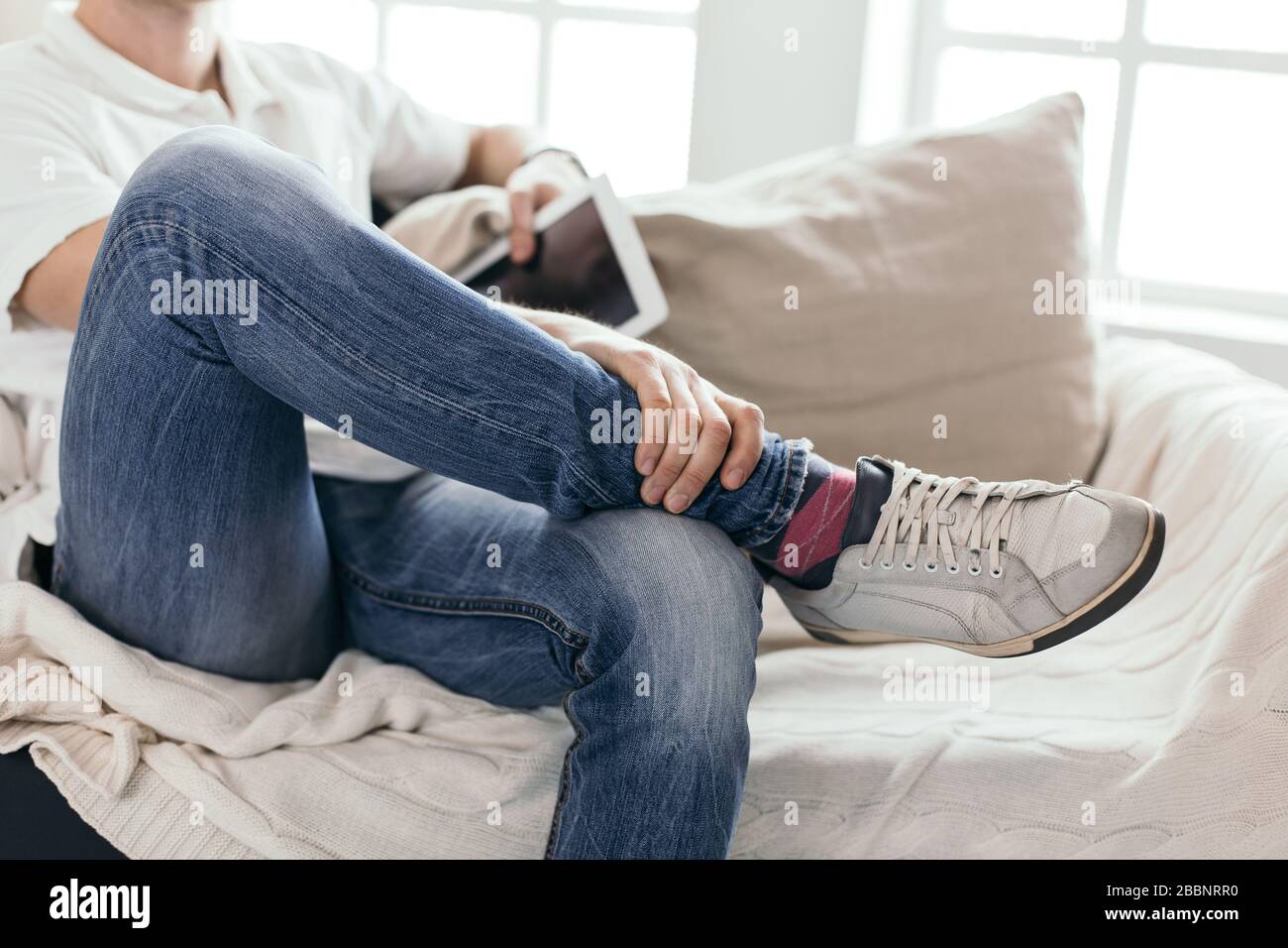 Junger Mann mit einem digitalen Tablett, das auf dem Sofa sitzt Stockfoto