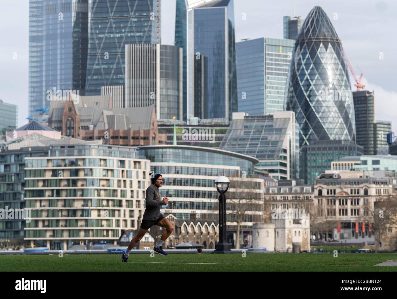 © 2020 Andrew Baker. LONDON GROSSBRITANNIEN. März 2020 EIN Jogger läuft durch einen leeren Potter Fields Park vor der Kulisse der City of London. Nach dem Stockfoto