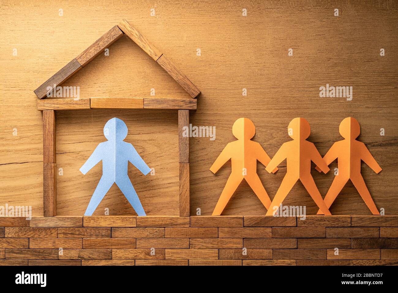 Blaue Papierausschnitte menschliche Figur in einem Holzblock, der nach Hause gebaut wurde, und drei weitere orangefarbene Papierausschnitte außerhalb des Holzhauses auf Holzrückenholz Stockfoto