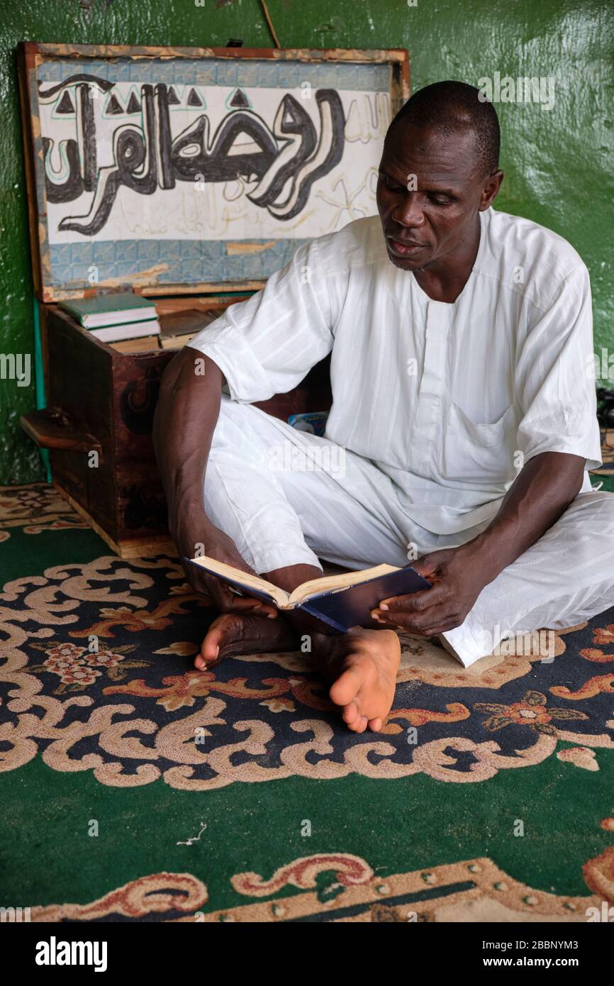 Muslimischer Mann, der auf dem Boden sitzt und den heiligen Koran liest. Stockfoto