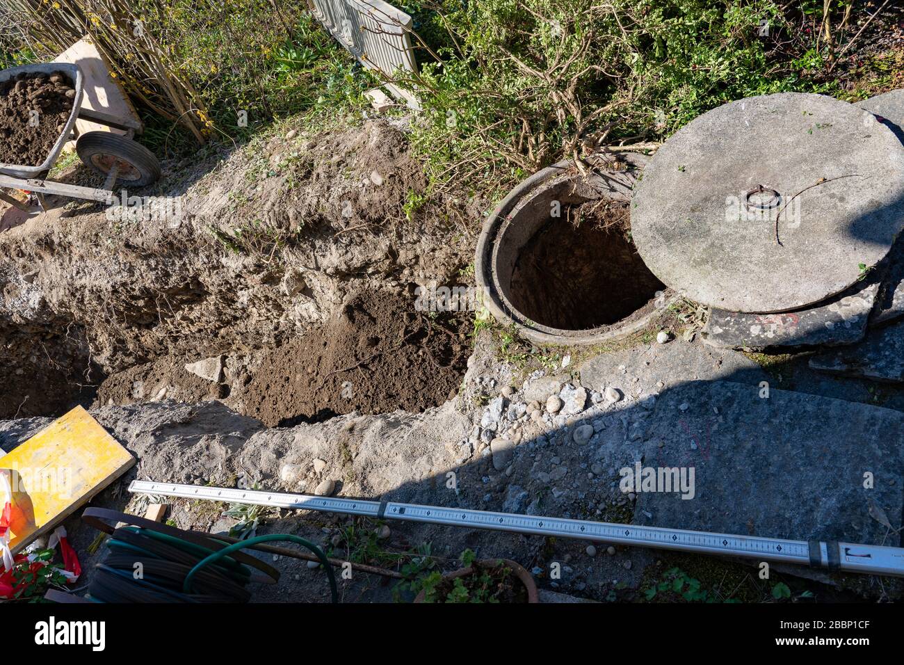 Blick auf die Baustelle des Abwasserschachts. Schubkarre gefüllt mit schwerem Boden, metrisches Maß auf dem Boden. Konzept. Stockfoto