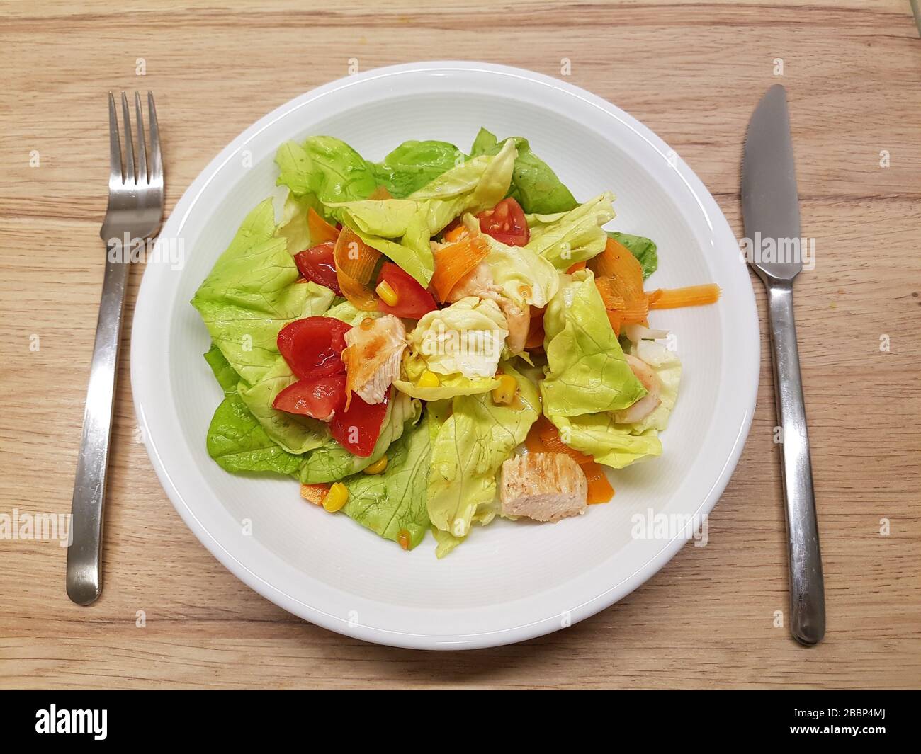 Gemischter grüner Salatsalat, Plattenbesteck, Holztisch, in Scheiben geschnittene Grüns, Gemüsesorten, Tomaten, geröstete Hühnerstücke - leicht, gesund Stockfoto