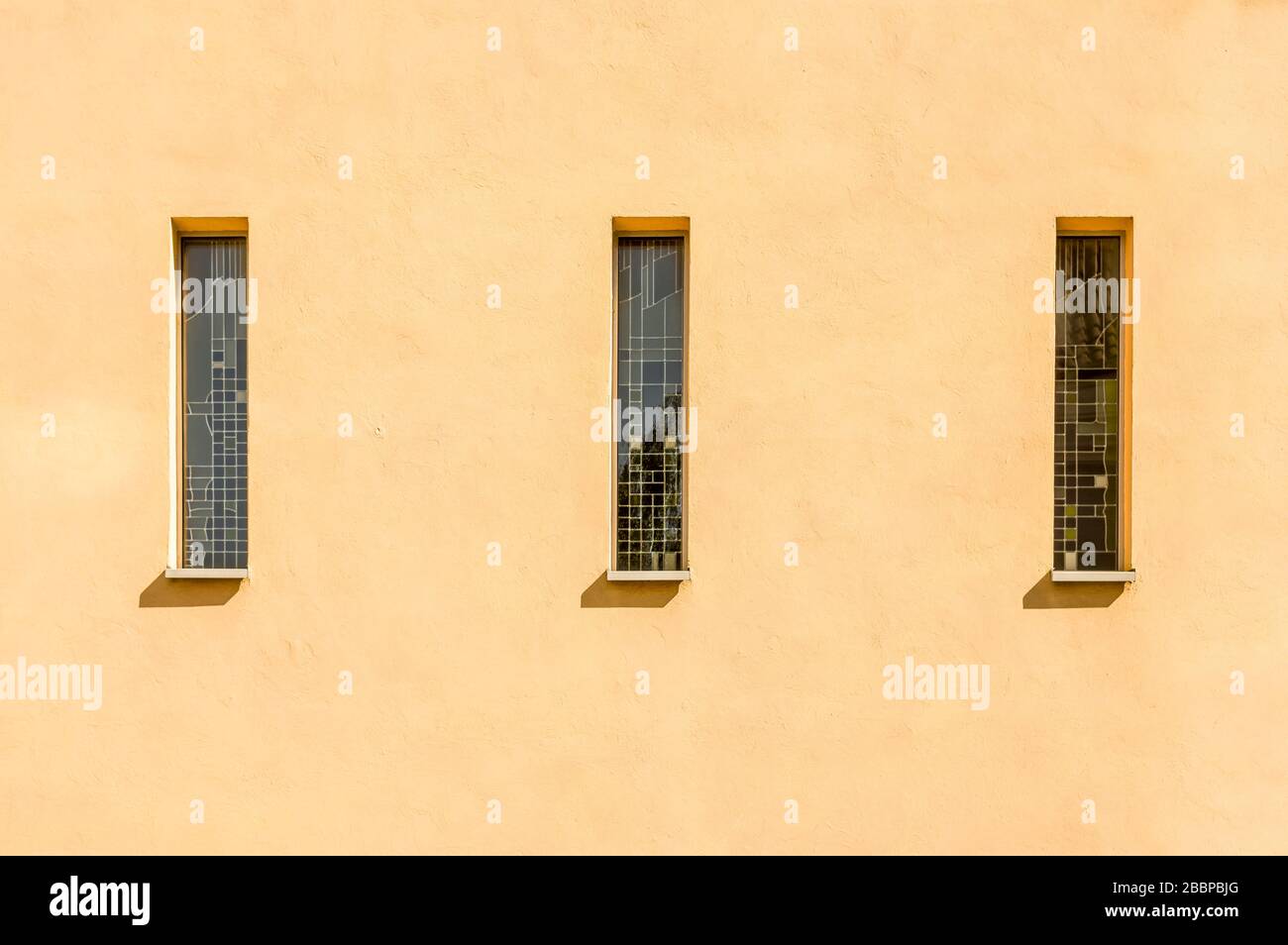 Symmetrische, ausgeschnittene moderne Fassade mit drei schmalen hohen Mosaikfenstern einer Kirche Stockfoto Symmetrische, ausgeschnittene moderne Fassade mit drei schmalen hohen Mosaikfenstern einer Kirche Stockfoto