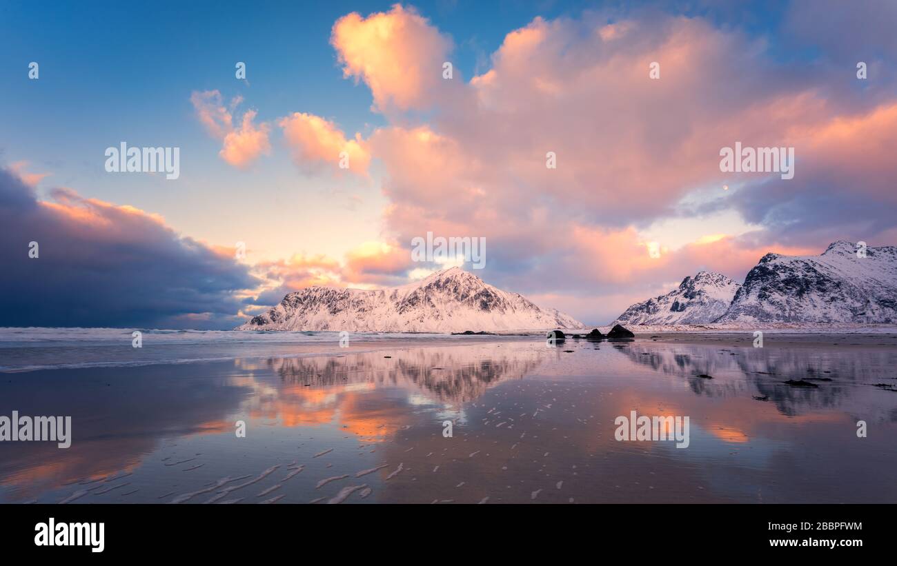 Der farbenfrohe Himmel spiegelte sich im Wasser am Strand mit schneebedeckten Bergen im Hintergrund wider Stockfoto