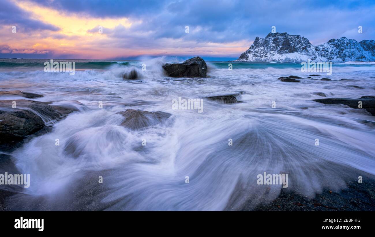 Ozeanwellen, die sich über Küstenfelsen waschen und im Hintergrund Himmel bei Sonnenuntergang aufschlagen Stockfoto