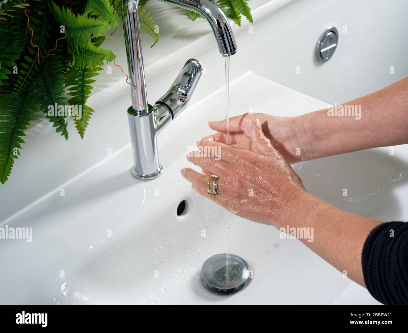 Eine Frau, die ihre Hände an einem Waschbecken waschen. Fließendes Wasser auf die Hände und das Becken dahinter klopfen. Badezimmer oder Toilette. Stockfoto