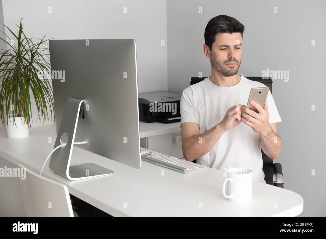 Ein Mann arbeitet von zu Hause aus mit seinem Telefon und Computer. Telearbeit-Konzept Stockfoto