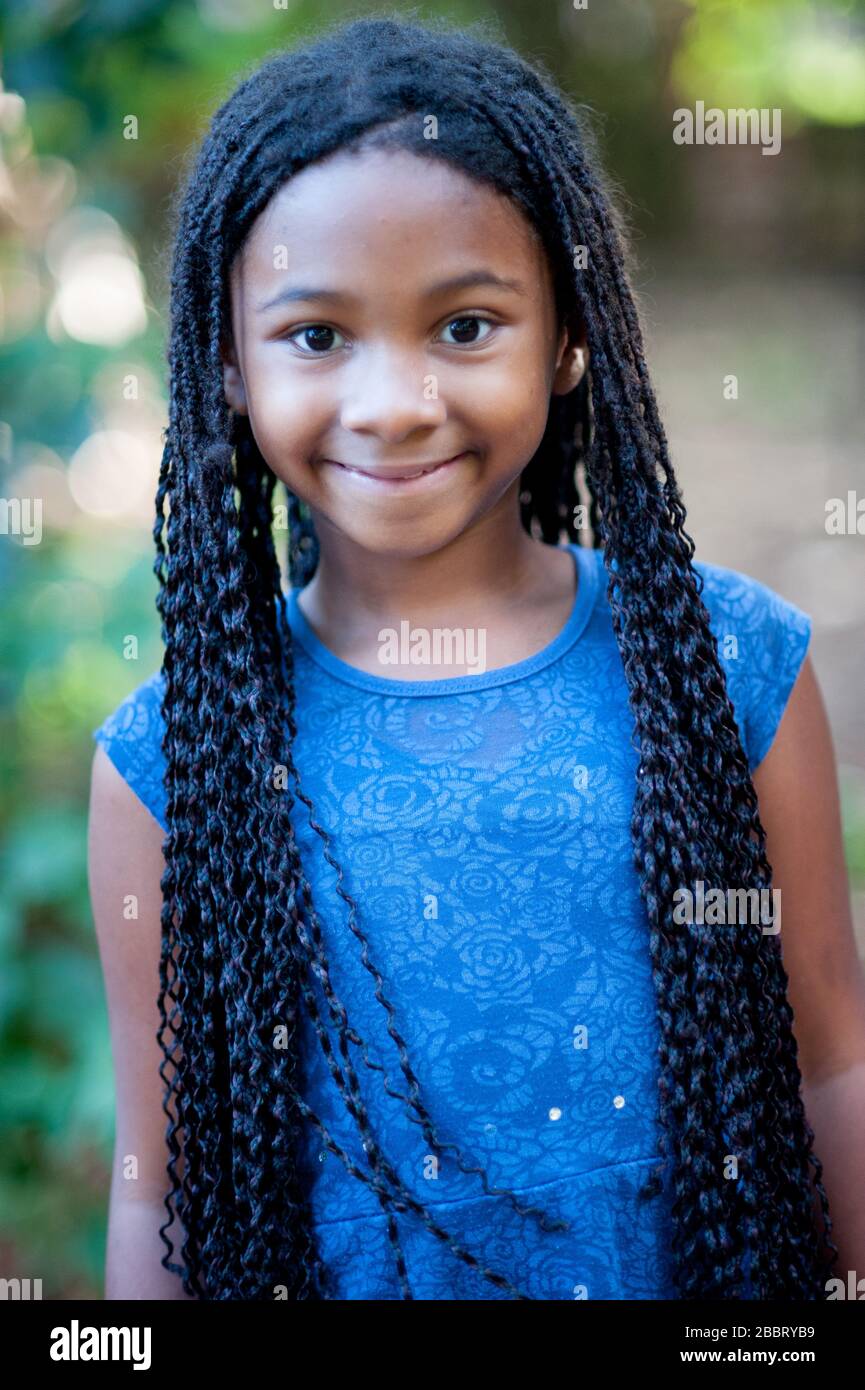 afro-amerikanisches Mädchen sieht die Kamera mit einem friedlichen Ausdruck aus. Sie hat langes schwarzes lockiges Haar. Fokus im Vordergrund. Stockfoto