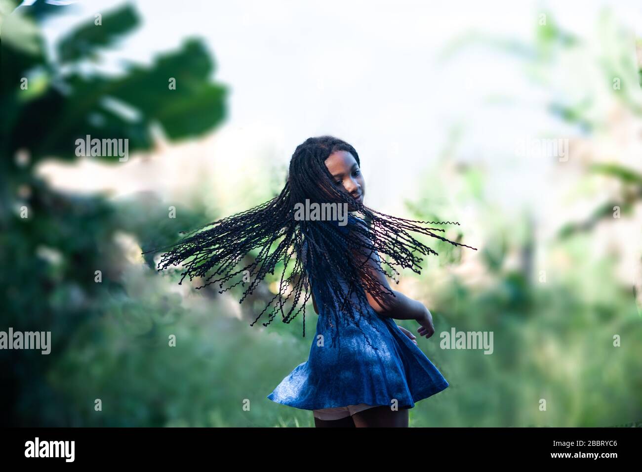 afro-amerikanisches Mädchen in der Natur, das ihr langes schwarzes Haar glücklich schwingt. Fokus auf Vordergrund. Stockfoto