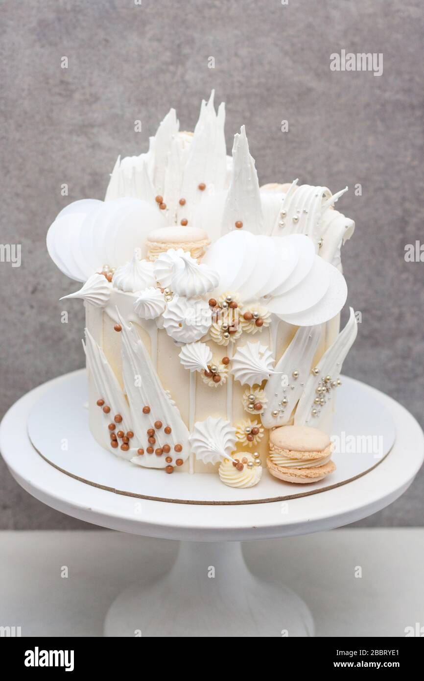 Moderner eleganter grauer Kuchen mit weißer Schokolade, Waffelpapier, Makronen und Meringues. Trendy eleganter Stil auf weißem Kakestand mit grauem Hintergrund. Stockfoto