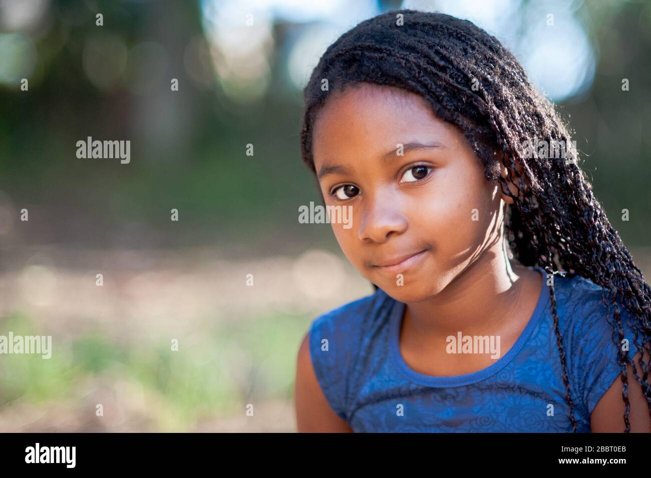 afro-amerikanisches Mädchen, das die Kamera mit einem friedlichen Ausdruck betrachtet. Fokus auf Vordergrund. Stockfoto