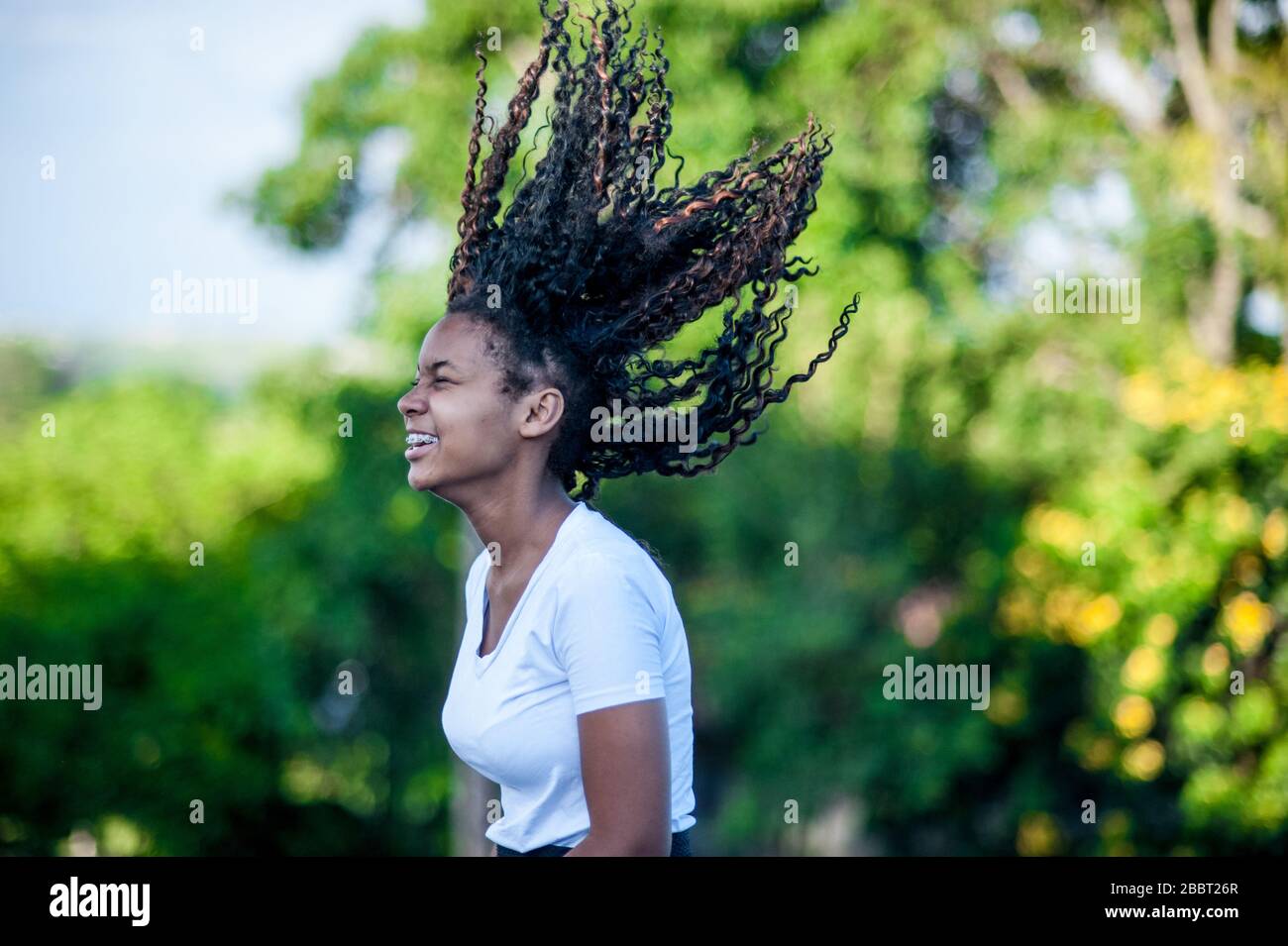 afroamerikanisches Mädchen lächelt und wirft ihr schwarzes Haar hoch. Fokus auf Vordergrund. Stockfoto