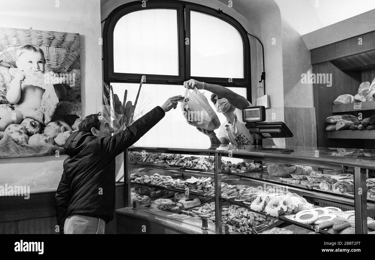 Rom, Italien. April 2020. Ein Assistent in einer Bäckerei, der eine Gesichtsmaske trägt, übergibt dem Kunden seine Einkäufe. Kredit: Stephen Bisgrove/Alamy Live News Stockfoto