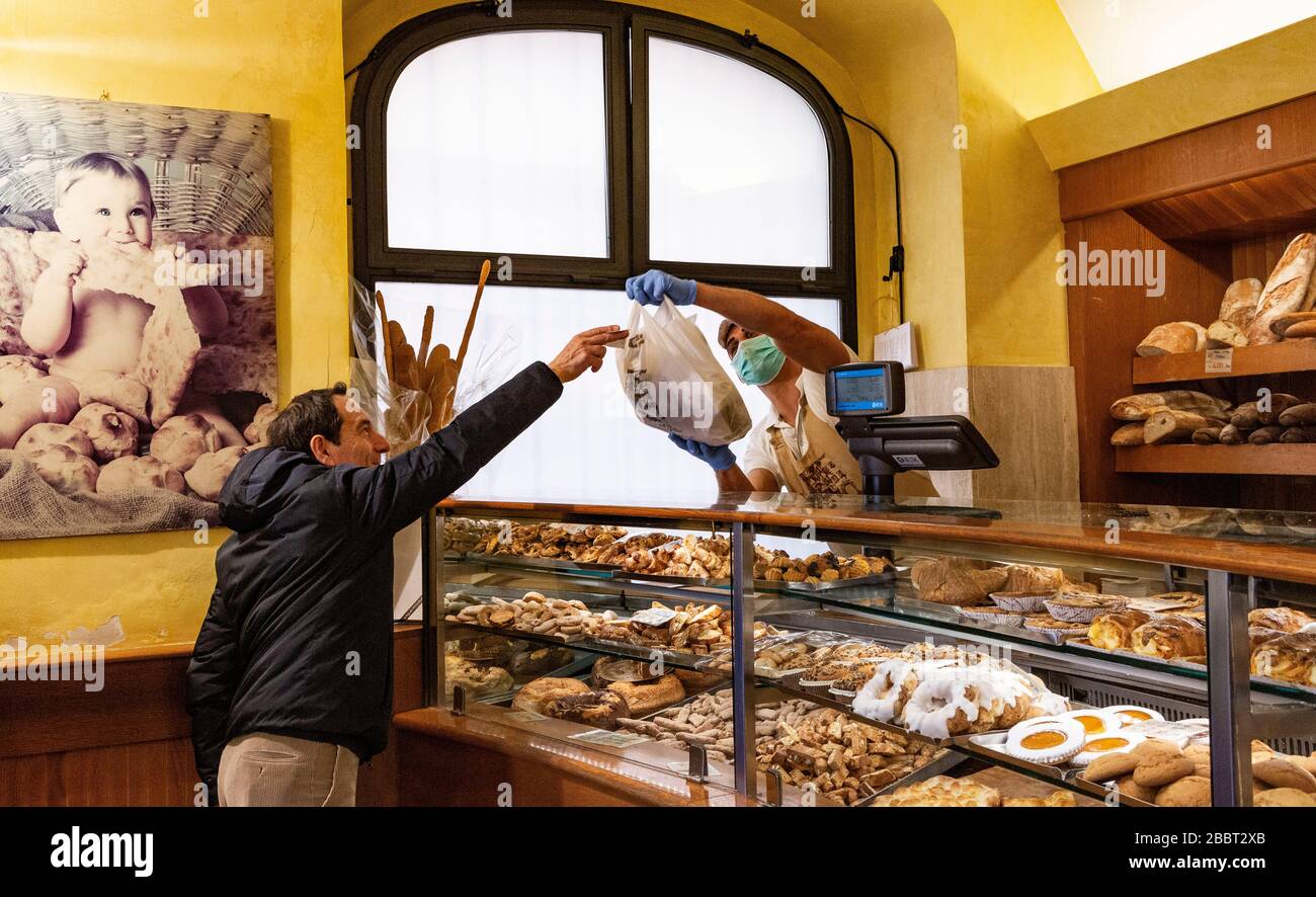 Rom, Italien. April 2020. Ein Assistent in einer Bäckerei, der eine Gesichtsmaske trägt, übergibt dem Kunden seine Einkäufe. Kredit: Stephen Bisgrove/Alamy Live News Stockfoto