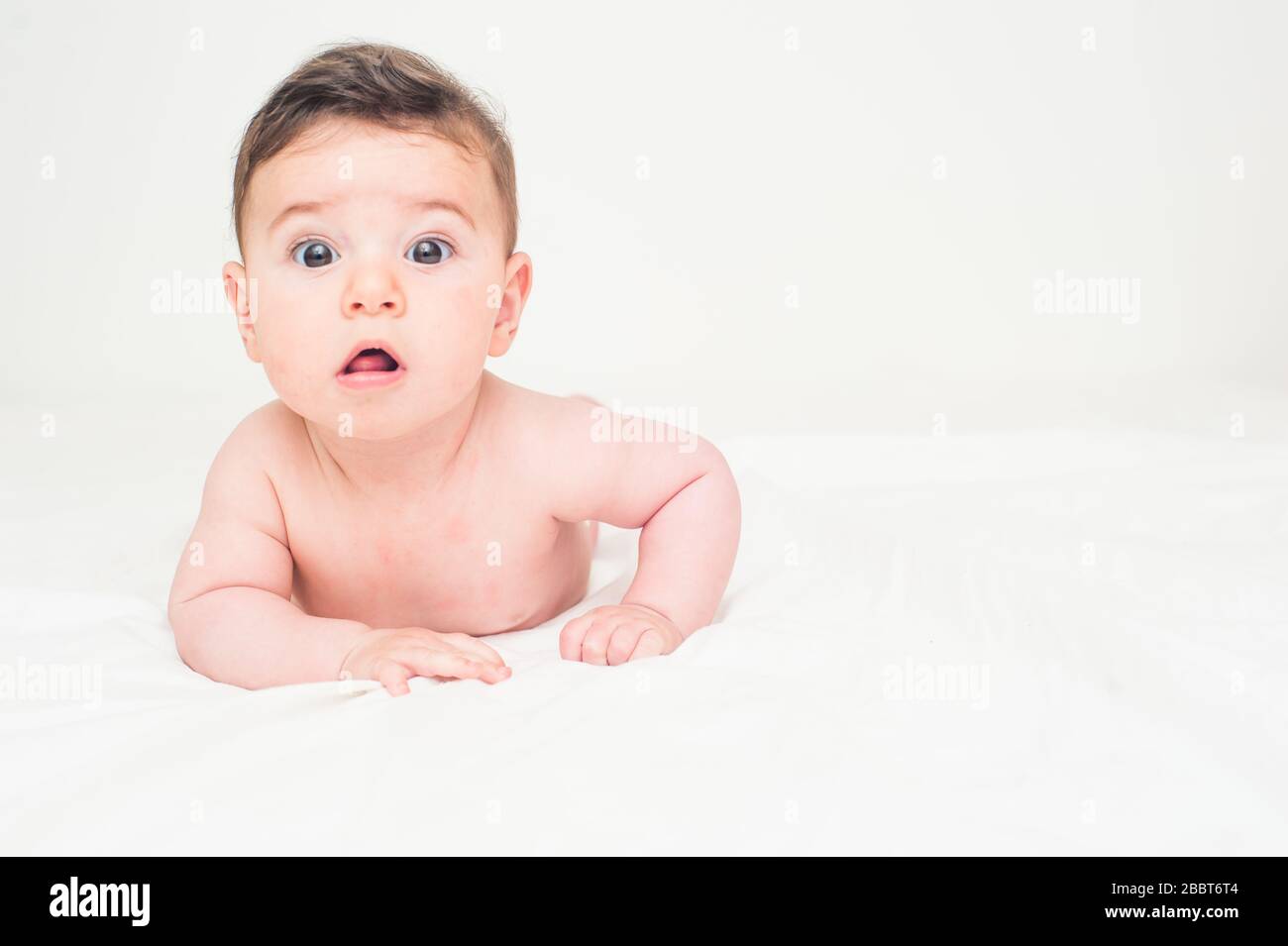 Süßes Baby liegt auf dem Bauch im Bett auf weißem Hintergrund. Bild mit großem Kopierraum. Stockfoto