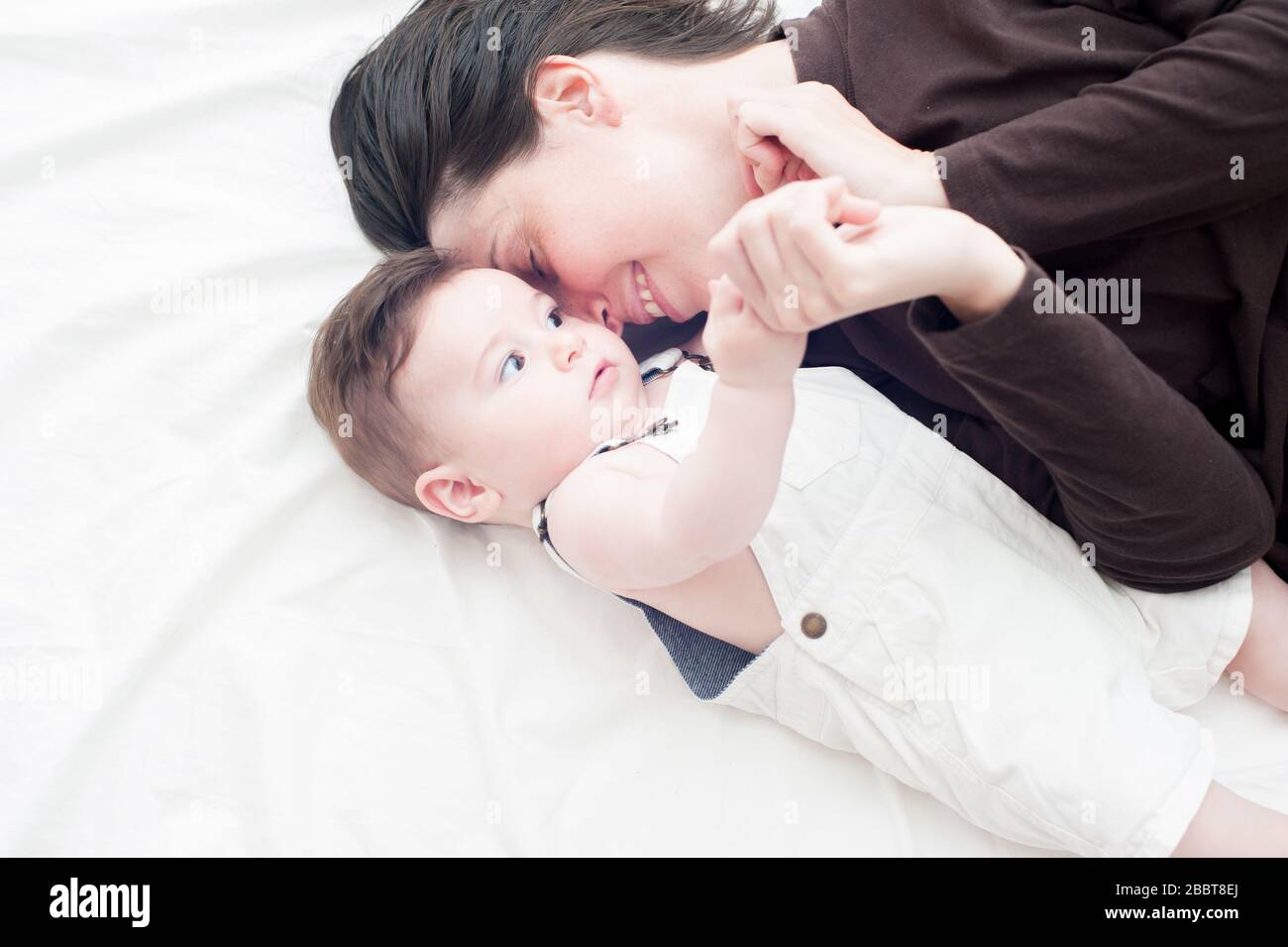 Echte glückliche Mutter hält ihr Baby sanft im Bett Stockfoto