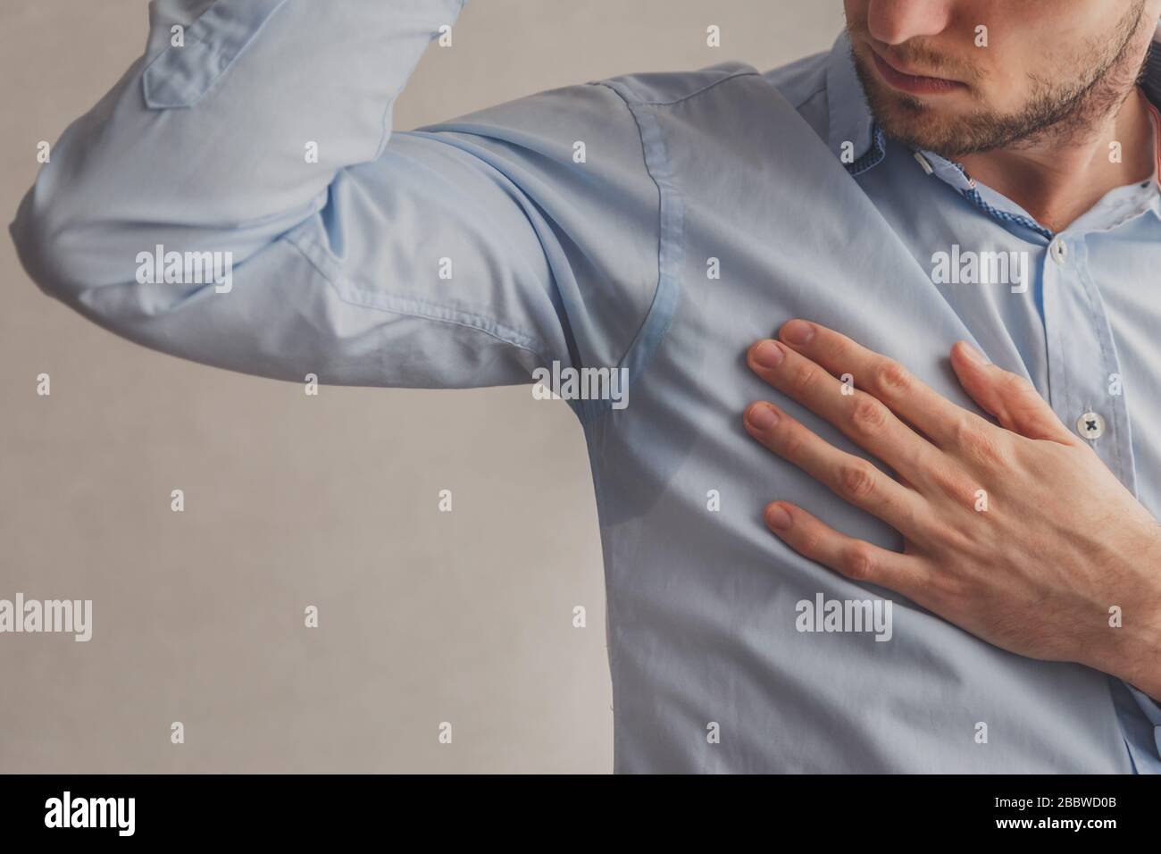 Mann mit Hyperhidrose schwitzt sehr schlecht unter Achselhöhlen in blauem Hemd, auf Grau. Stockfoto