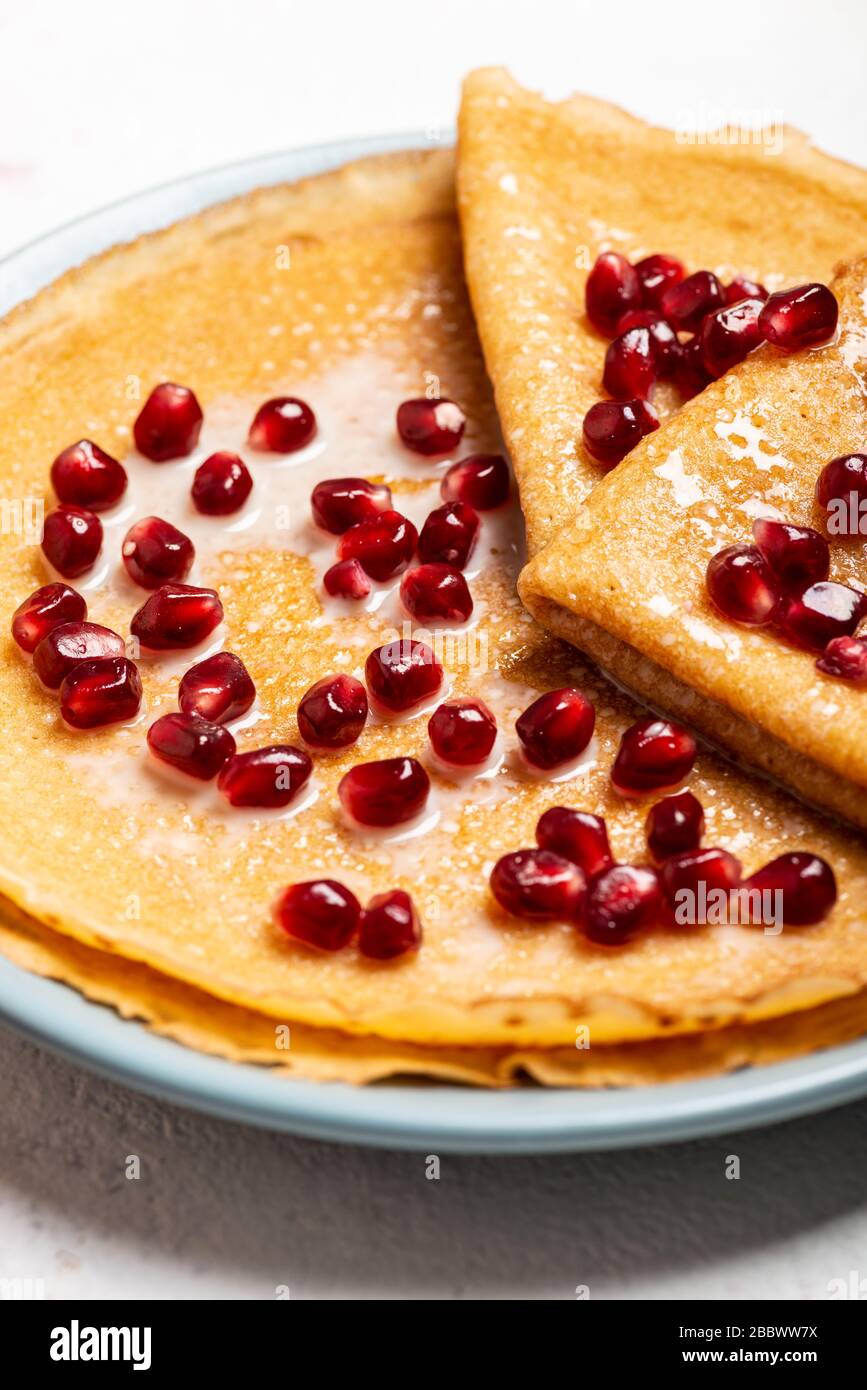 Pfannkuchen mit Granatapfel und Kondensmilch liegen auf einem Teller. Makro. Draufsicht. Stockfoto