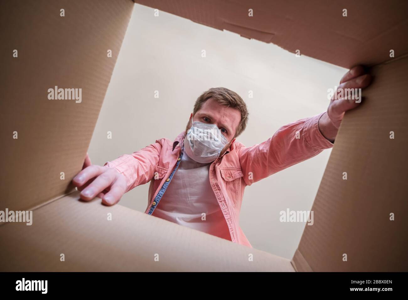 Mann in einer medizinischen Maske Auspacken im Inneren einer gelieferten Schachtel. Konzept von Paranoia und Hysterie im Zusammenhang mit einem Epidemievirus. Stockfoto