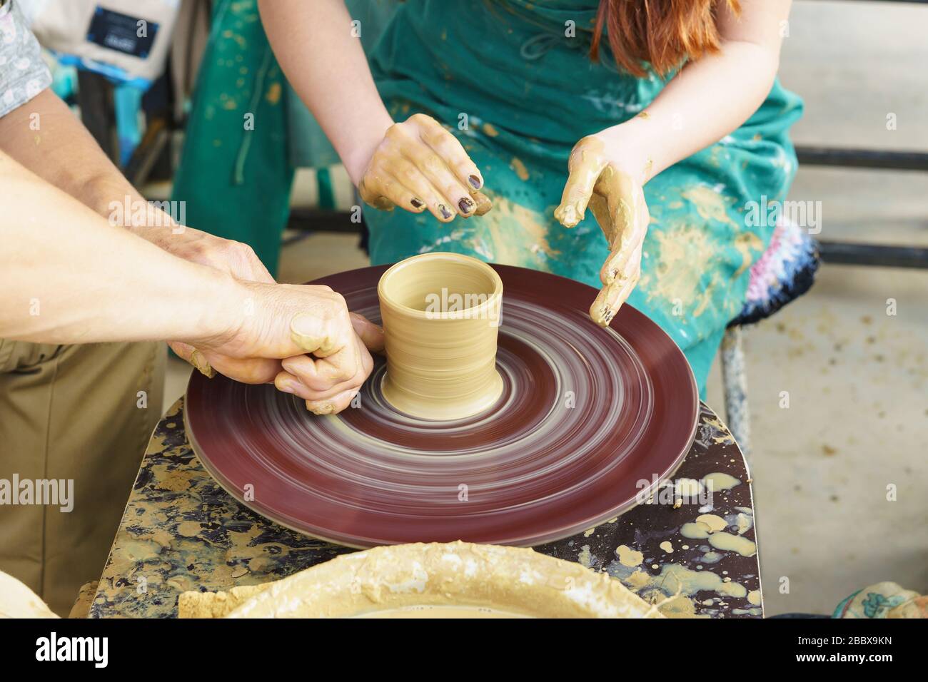 Die Hände eines Meisters und eines Studenten machen einen Krug auf einem Potter-Rad aus gelbem Ton. Selektive Fokussierung auf die Hände Stockfoto