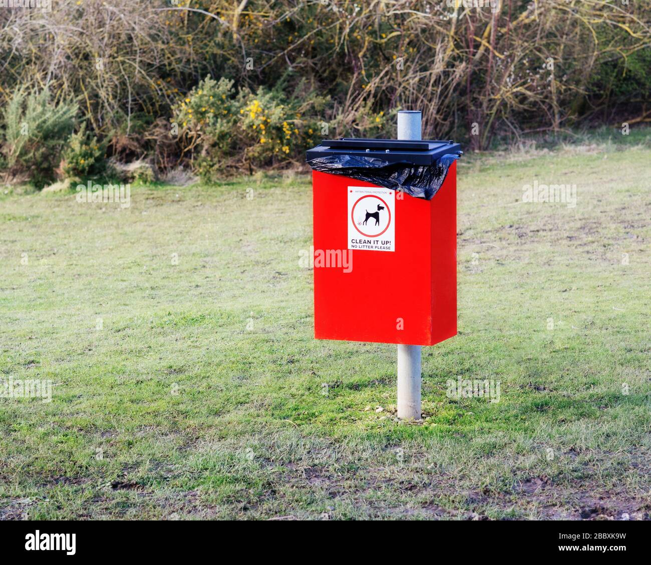 Roter Mülleimer für Hundeeinwurf mit Schild reinigt es und ein Bild eines Hundes im Park Stockfoto