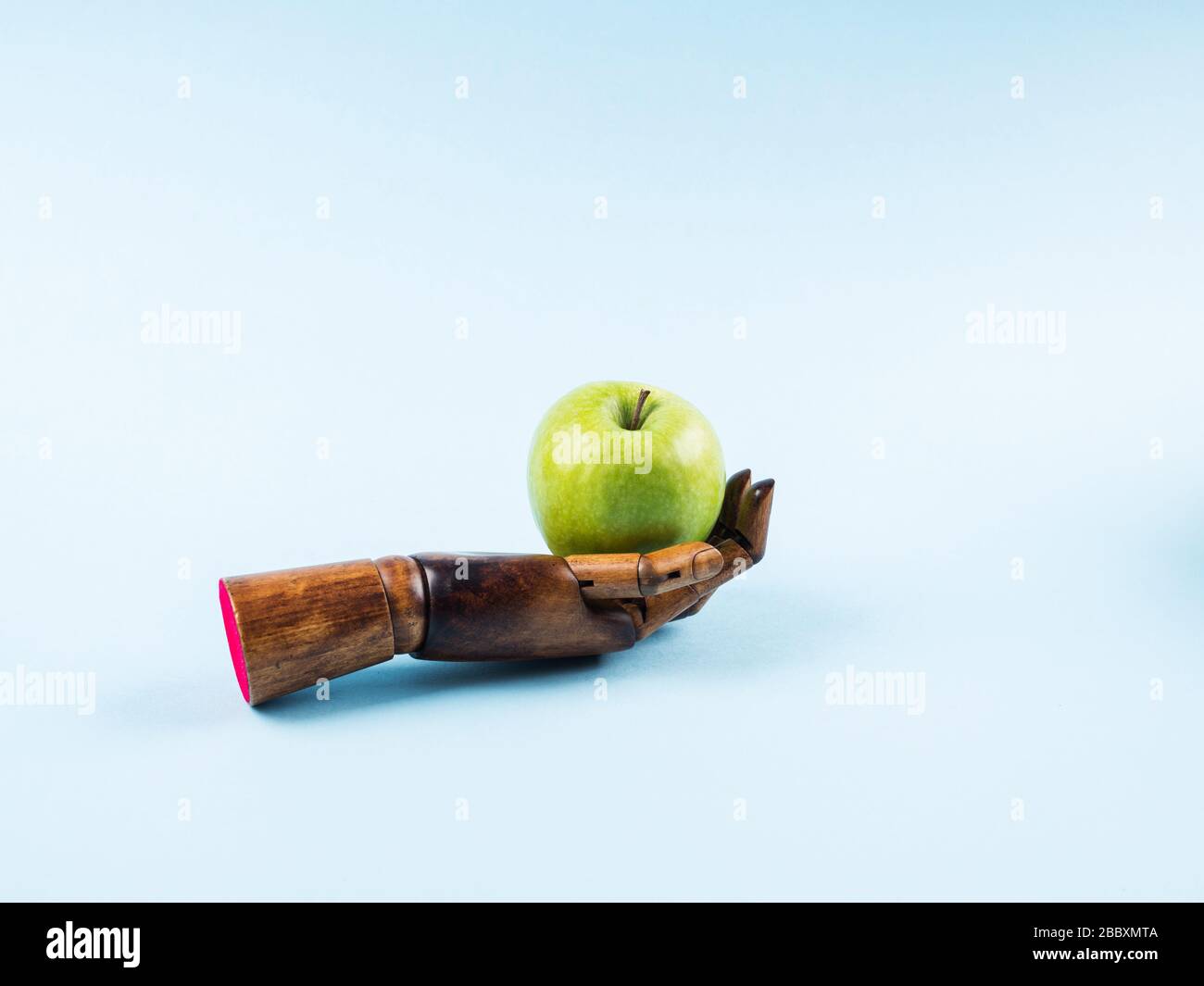 Frischer grüner apfel in der Palme aus Holzhand auf Blau Stockfoto