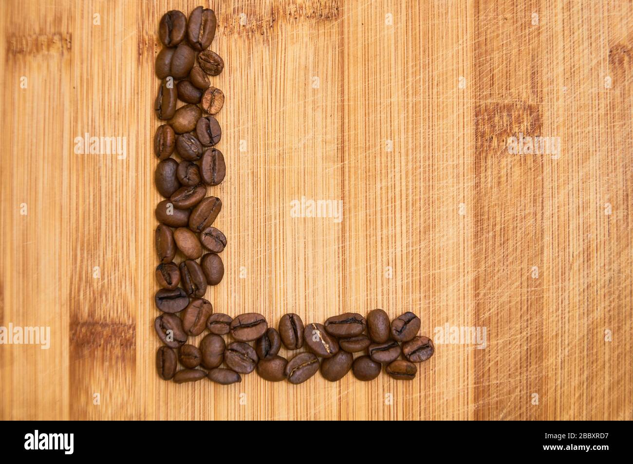 Buchstaben L aus gerösteten Kaffeebohnen, 3D-Rendering auf Holztischhintergrund Stockfoto