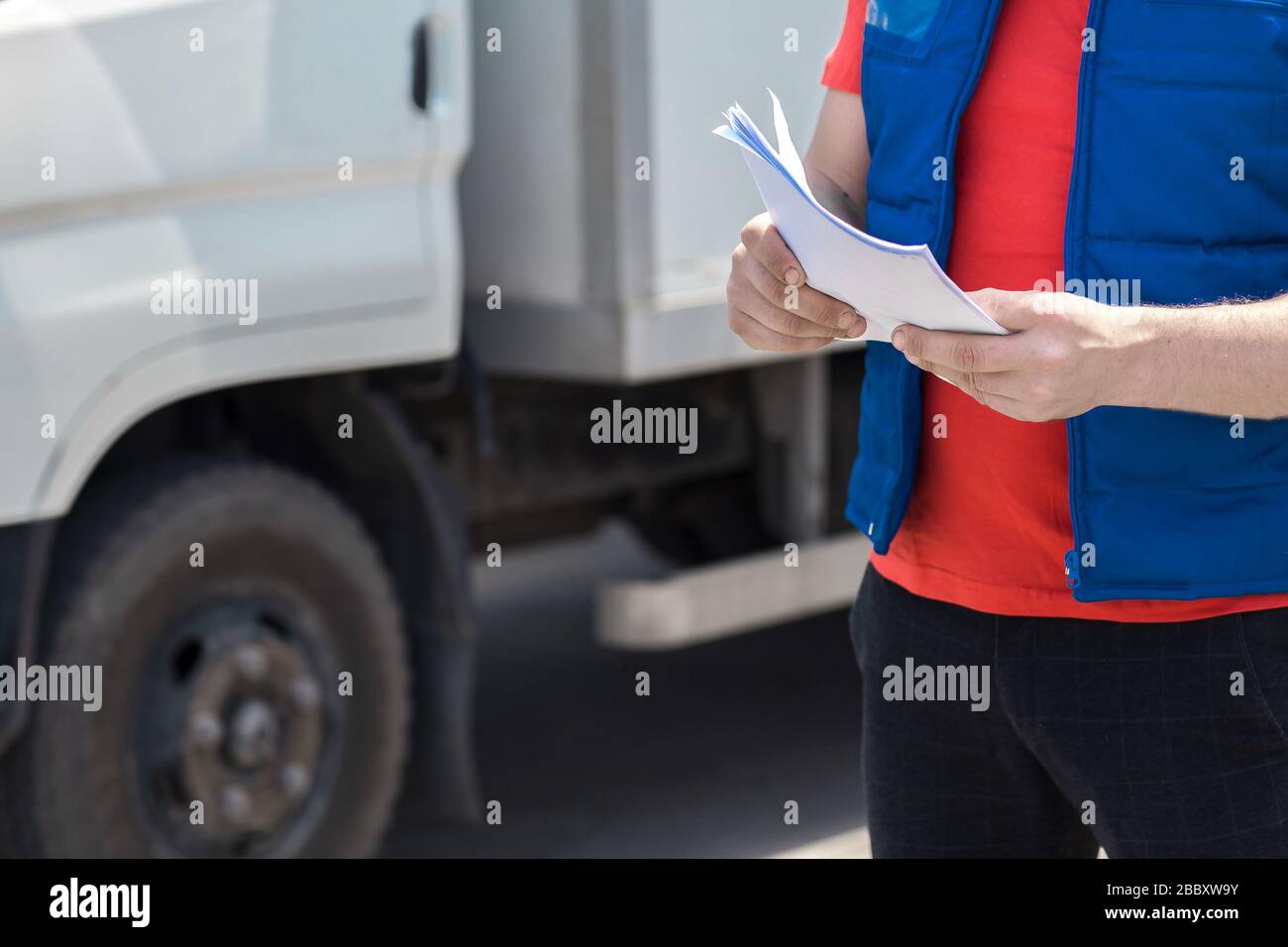 Kurierfahrer in Uniform macht Notizen in Dokument und Lieferung weißer LKW behinde ihn Stockfoto