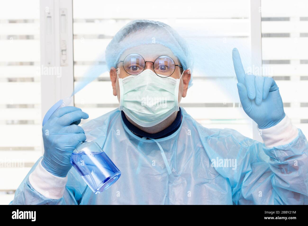 Arzt im Schutzanzug, der antibakterielles Aerosol aus der Flasche sprüht. Medizinisches Personal zeigt ein Desinfektionsmittel. Stockfoto