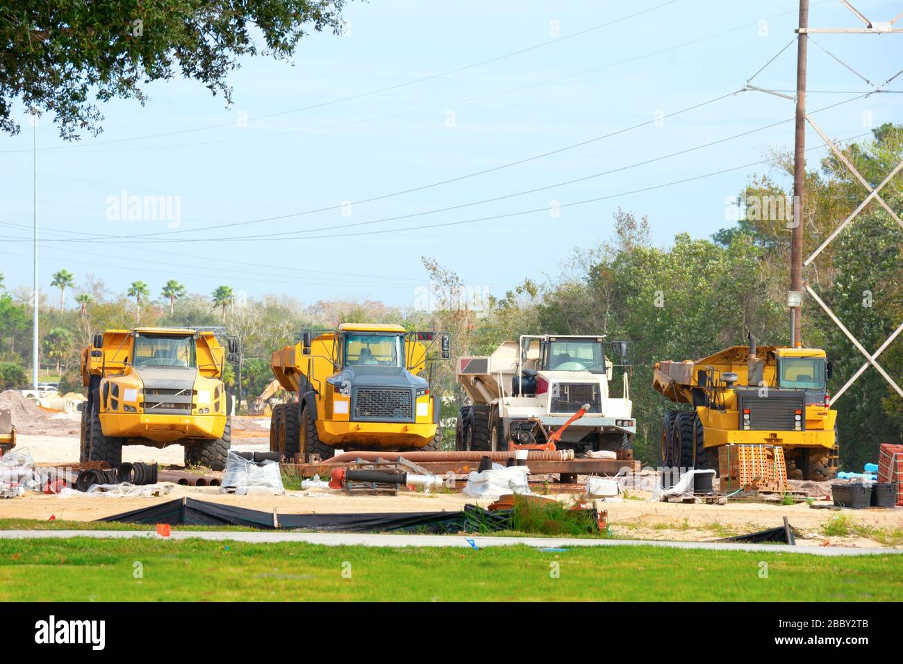 Reihe von Arbeitskippwagen, die in einer Reihe auf dem Bauzonengelände mit gerodeten Flächen und vorgerödeten Baumreihen im Hintergrund geparkt wurden. Stockfoto
