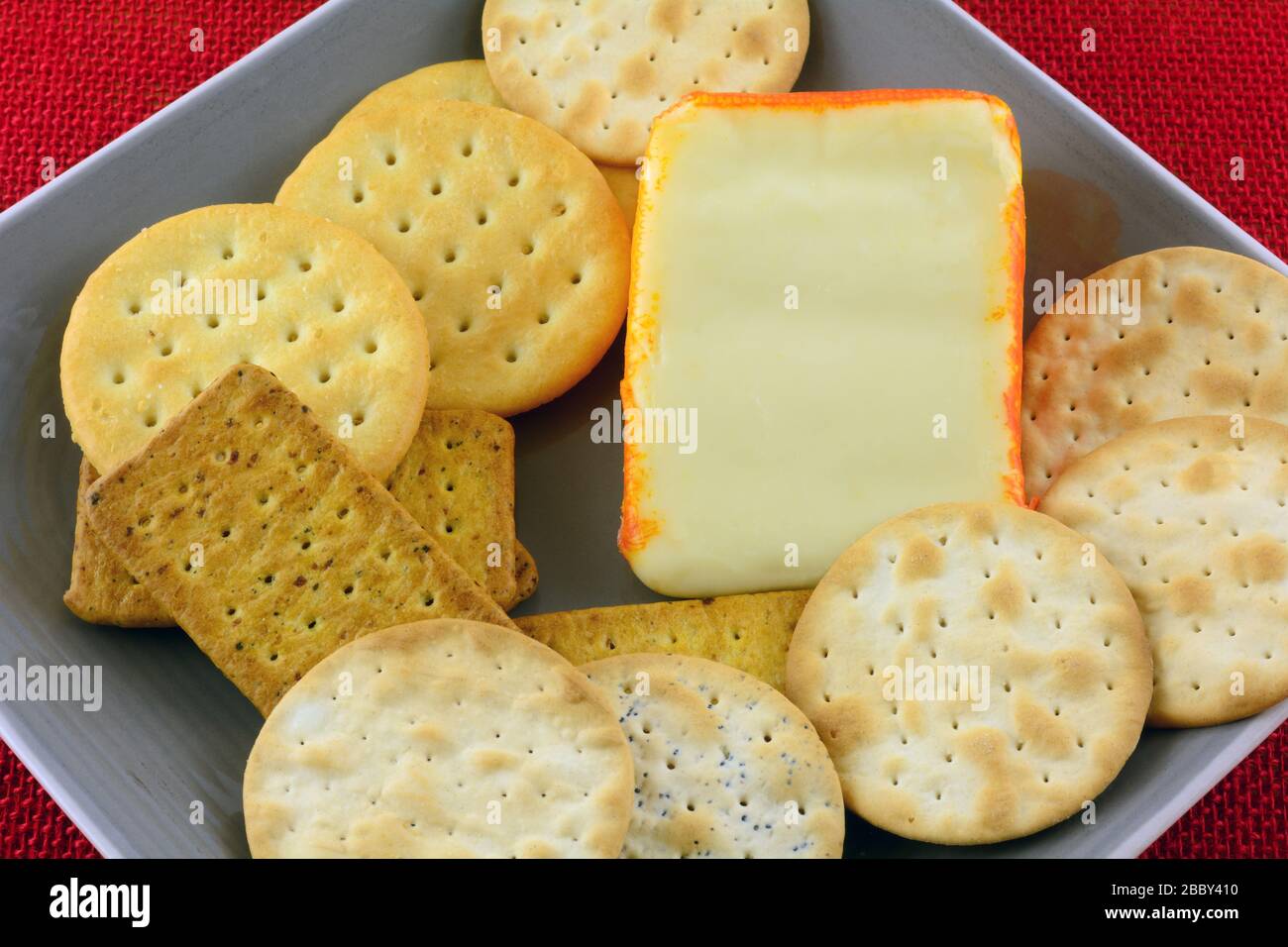 Nahaufnahme des Keils von Port Salut halbweicher Käse auf Platte mit verschiedenen Crackern Stockfoto