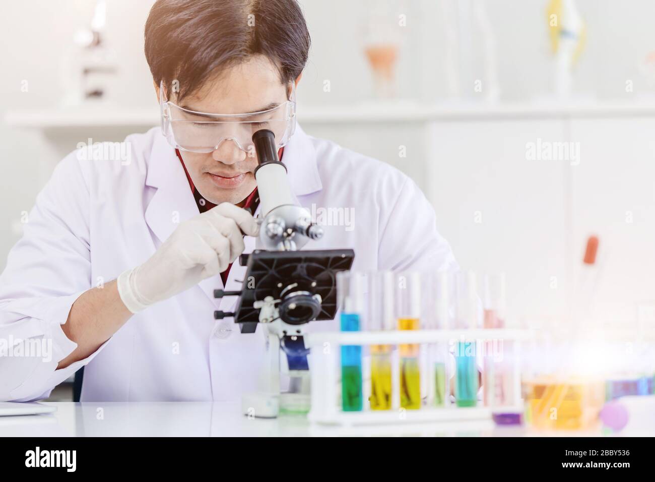 Asiatischer Wissenschaftler, der im medizinischen Gesundheitslabor für wissenschaftliche medizinische Forschung mit Mikroskop arbeitet Stockfoto