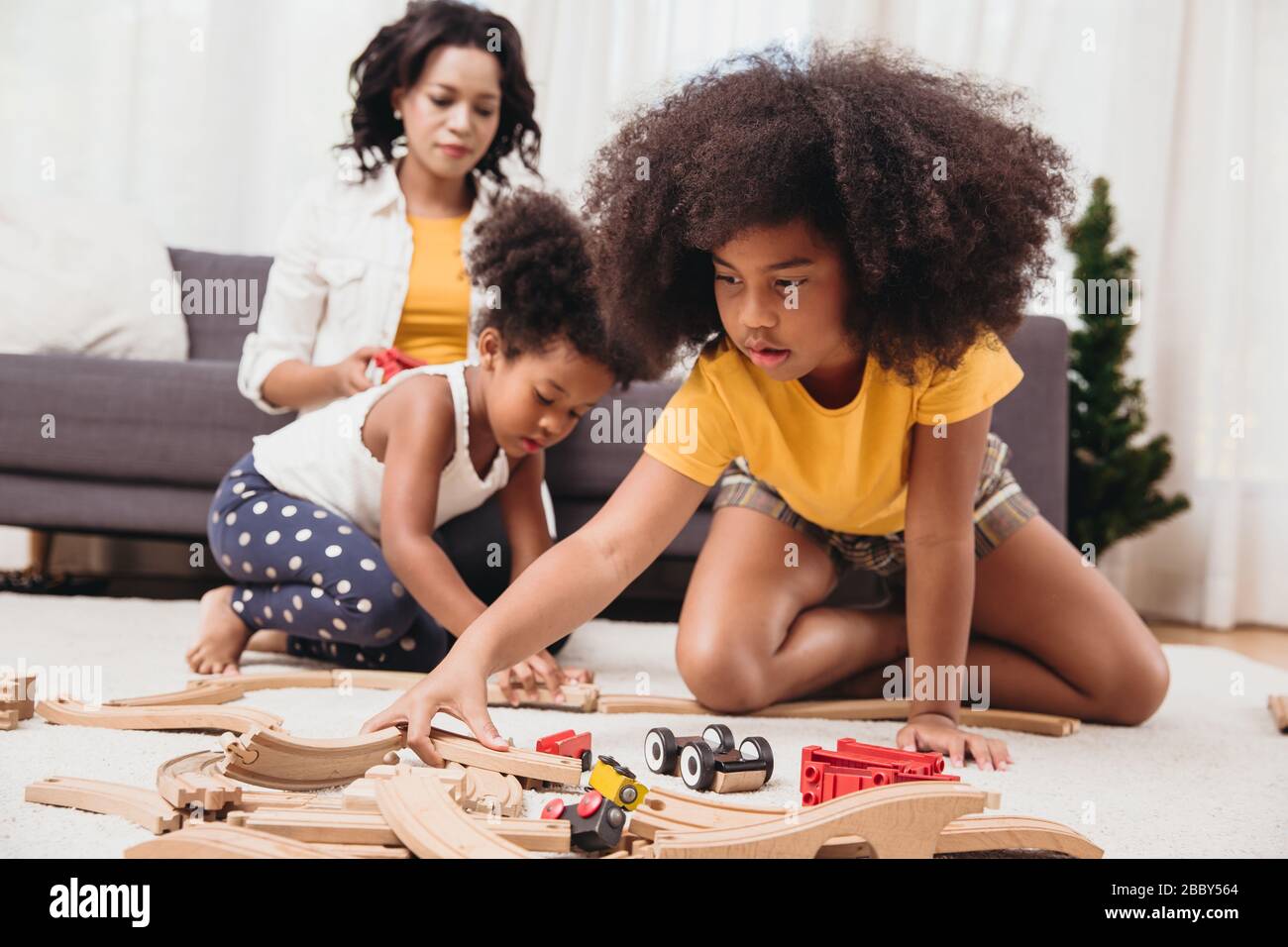 Alleinerziehende Mutter mit zwei Tochter, die in der Wohnung Spielzeug spielt. Kindermädchen, die zu Hause schwarze Menschen suchen oder sich um eine Kinderbetreuung scheren. Stockfoto