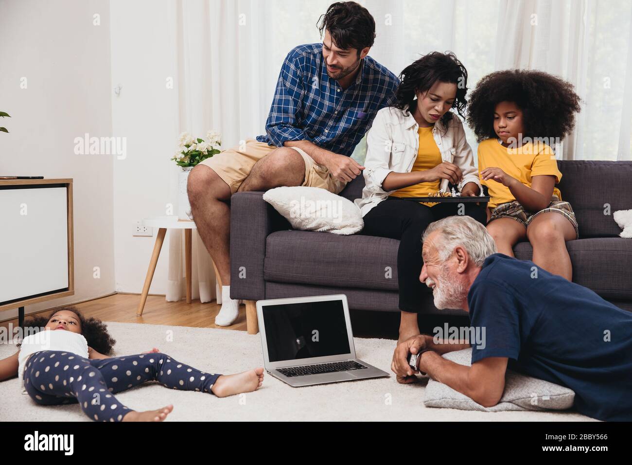 Schönes Zuhause Familie bleiben Sie zusammen im Wohnzimmer Vater Mutter und Großvater spielen mit Tochter Mix Race. Stockfoto