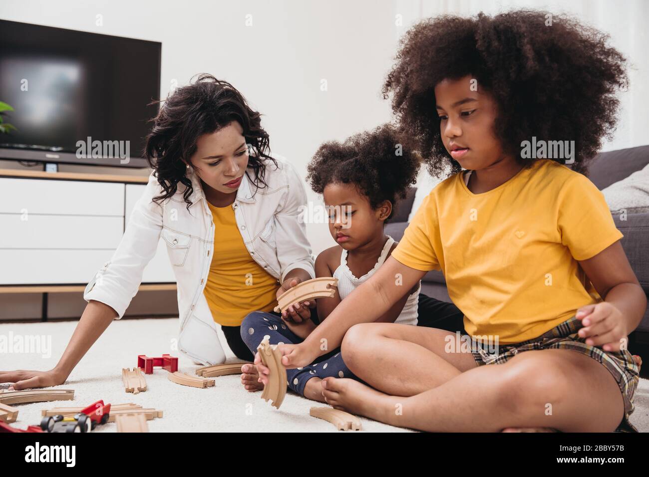 Alleinerziehende Mutter mit zwei Tochter, die in der Wohnung Spielzeug spielt. Kindermädchen, die zu Hause schwarze Menschen suchen oder sich um eine Kinderbetreuung scheren. Stockfoto