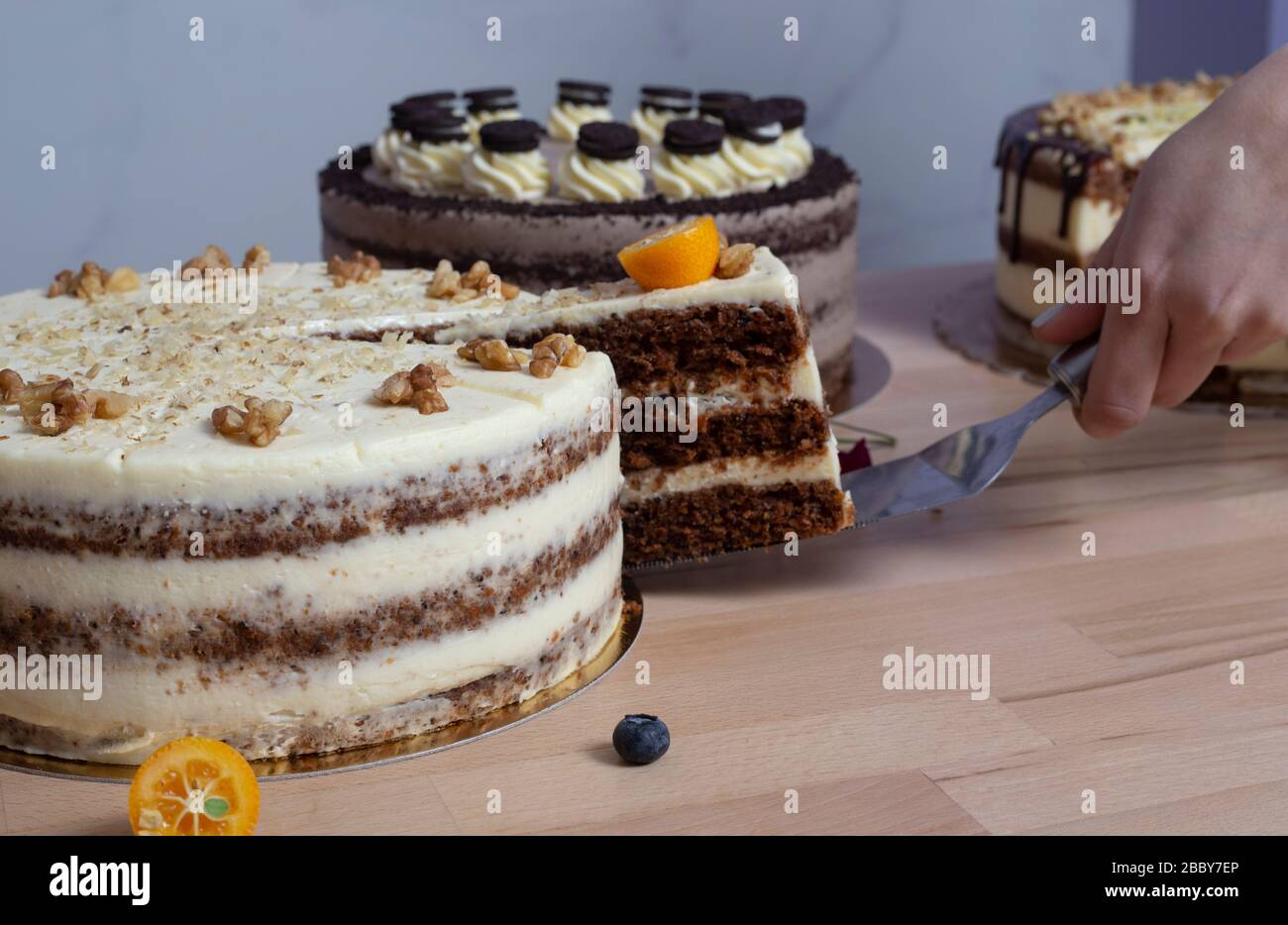 Die Hände der Frau fangen ein Stück Kuchen mit weißer Schokolade auf Holztischhintergrund. Auswahl an Festkuchen. Stockfoto