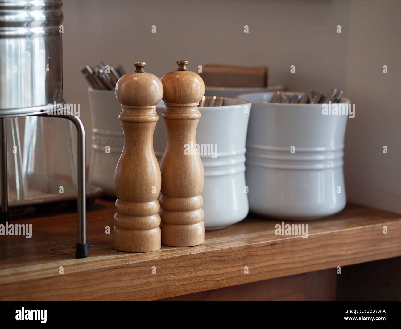 Holzhandkurbel mit Salz und Pfefferschüttler auf dem Tisch mit Utensilien in Keramiktöpfen Stockfoto